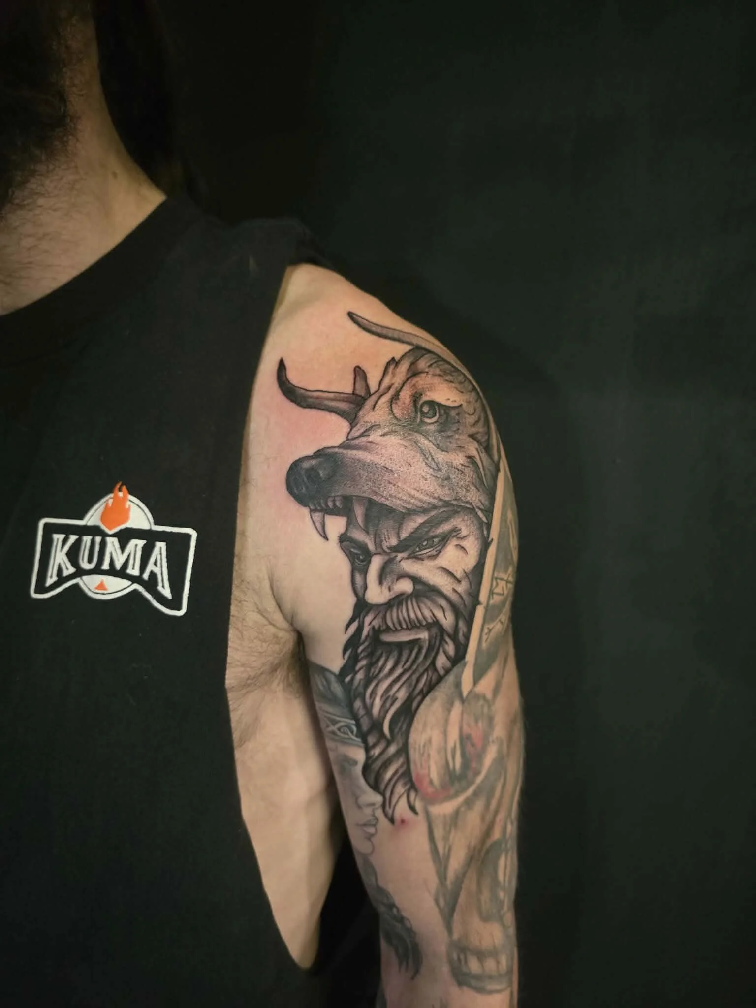 Tattoo of a Viking warrior with a long beard and a horned helmet, combined with a dog's head, on a person's upper arm and shoulder.
