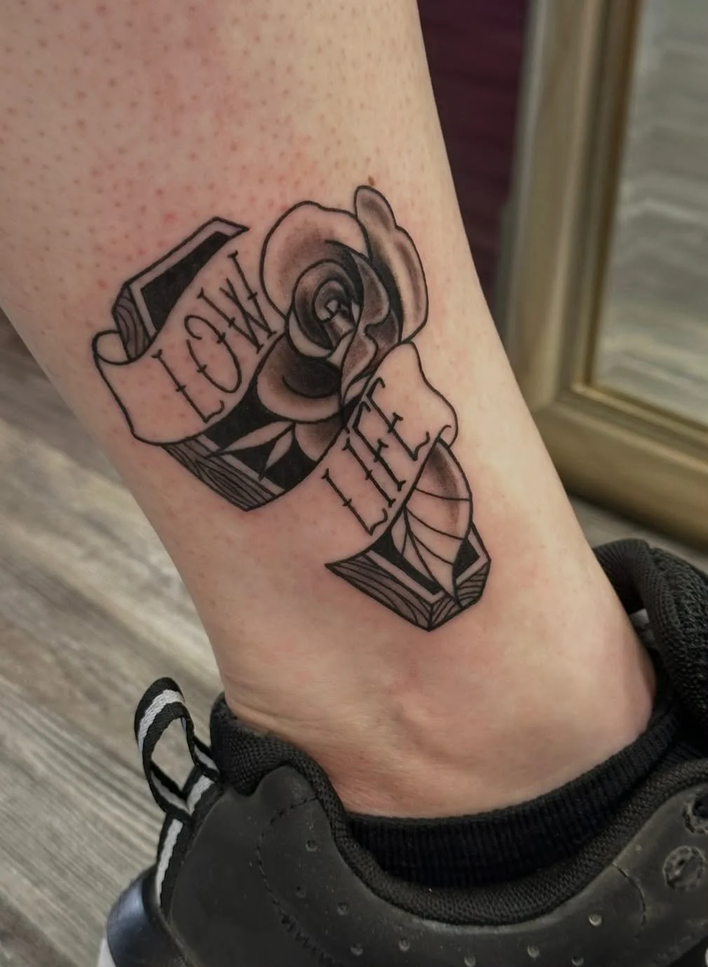 Tattoo of a rose with a ribbon wrapped around it. The ribbon has the words 'Love Life' written on it.