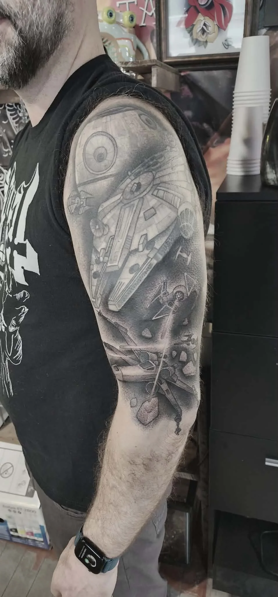 Tattoo of a space scene with Star Wars spacecraft, including the Millennium Falcon, among asteroids and stars, on a person's upper arm.