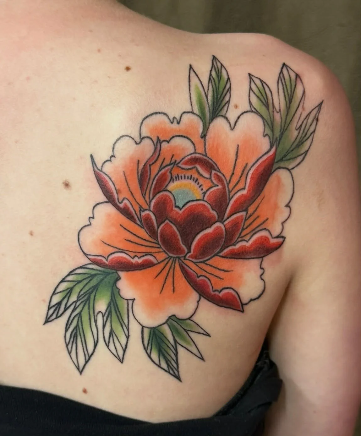 Colorful tattoo of a large orange and red flower with green leaves on a person's shoulder.