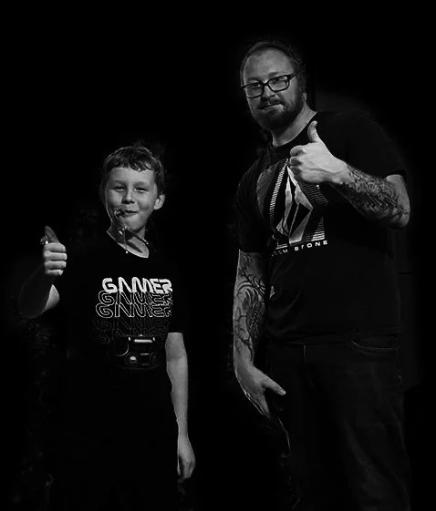 A boy and a man giving thumbs up, both smiling and standing against a dark background.