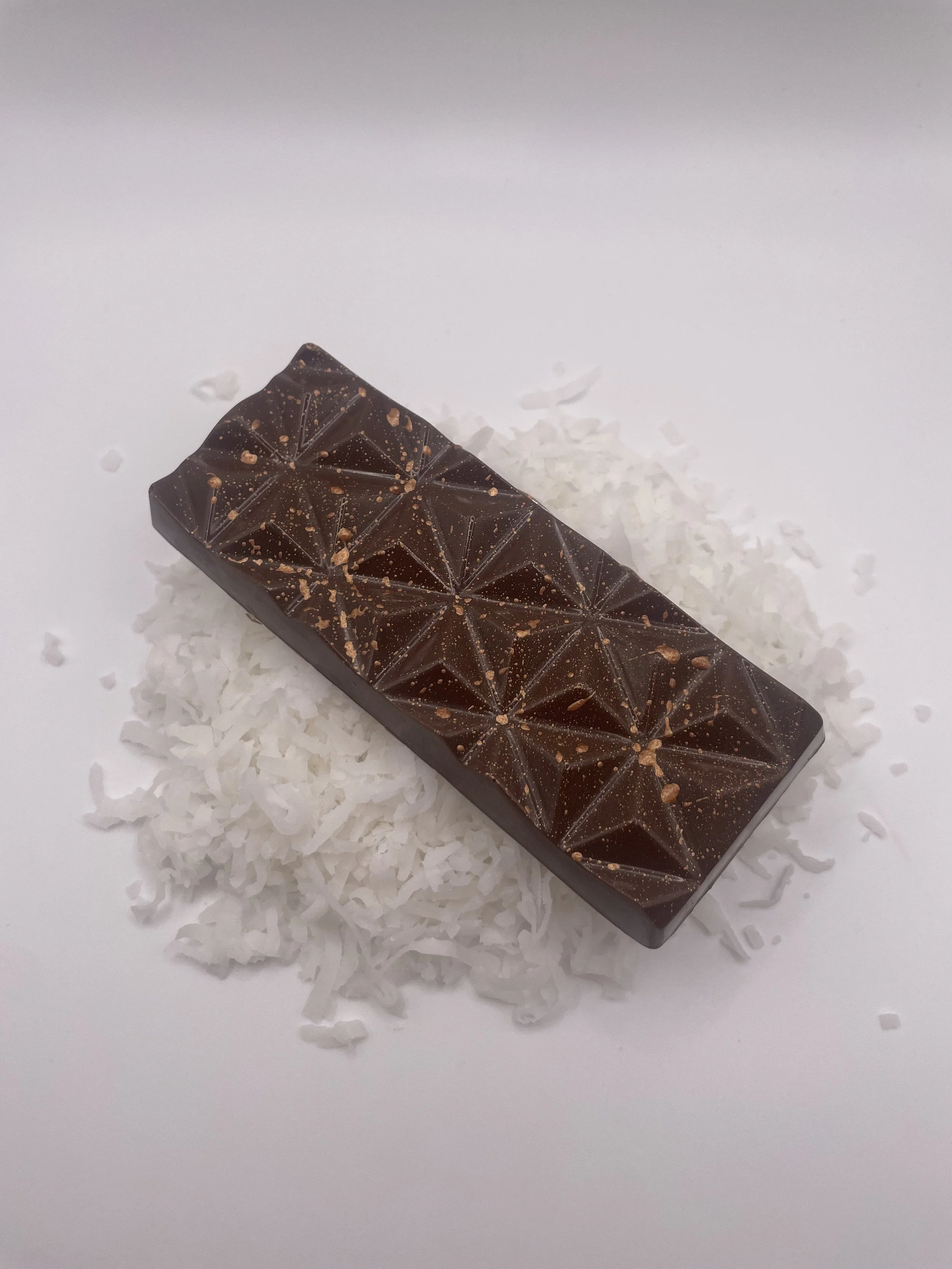 Chocolate praline bar with geometric patterns on top, surrounded by shredded coconut on a white background.