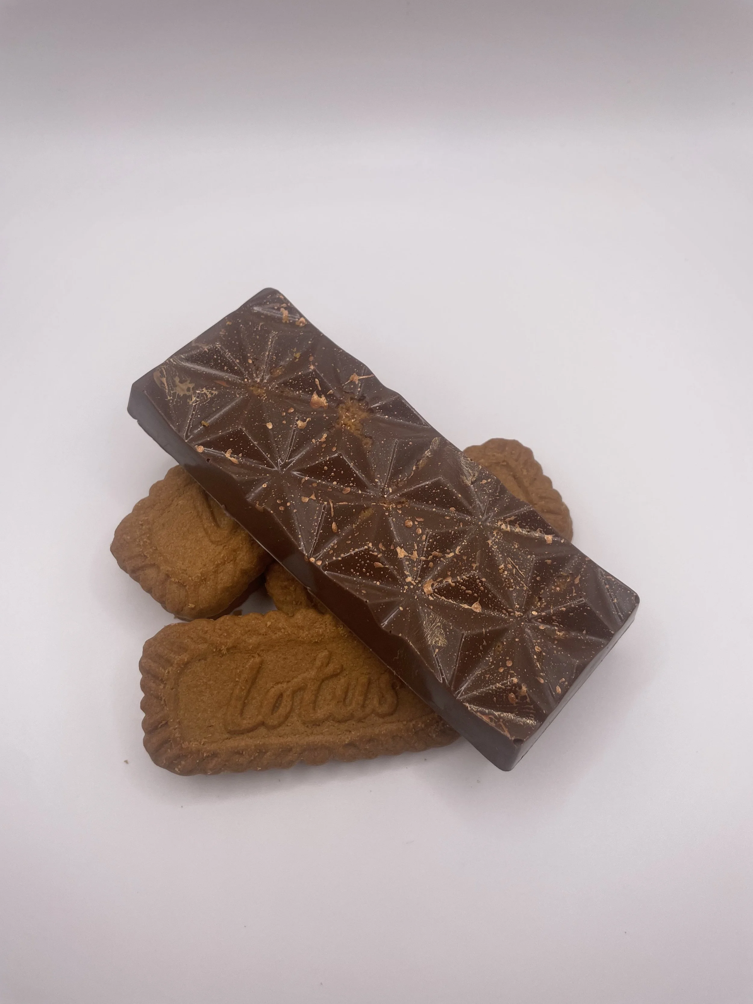 Two Amandus cookies topped with a bar of dark chocolate on a white surface.