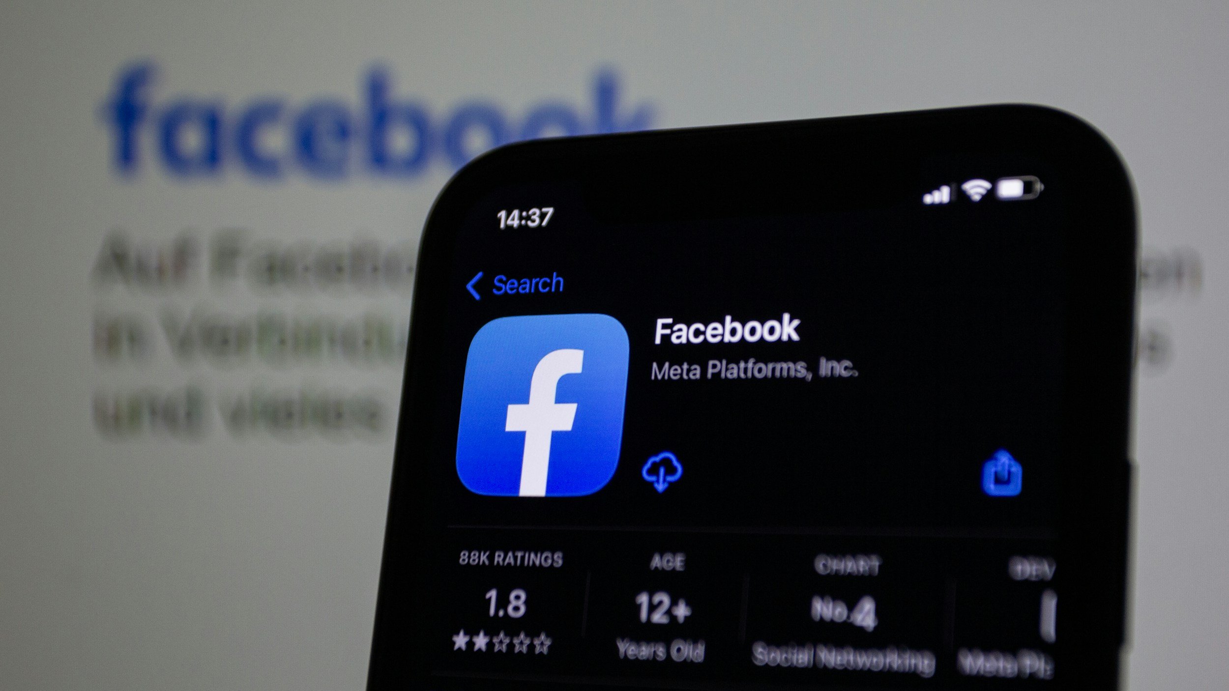 A smartphone screen displaying the Facebook app page with logo, ratings, age, and other details, with a blurred Facebook webpage in the background.
