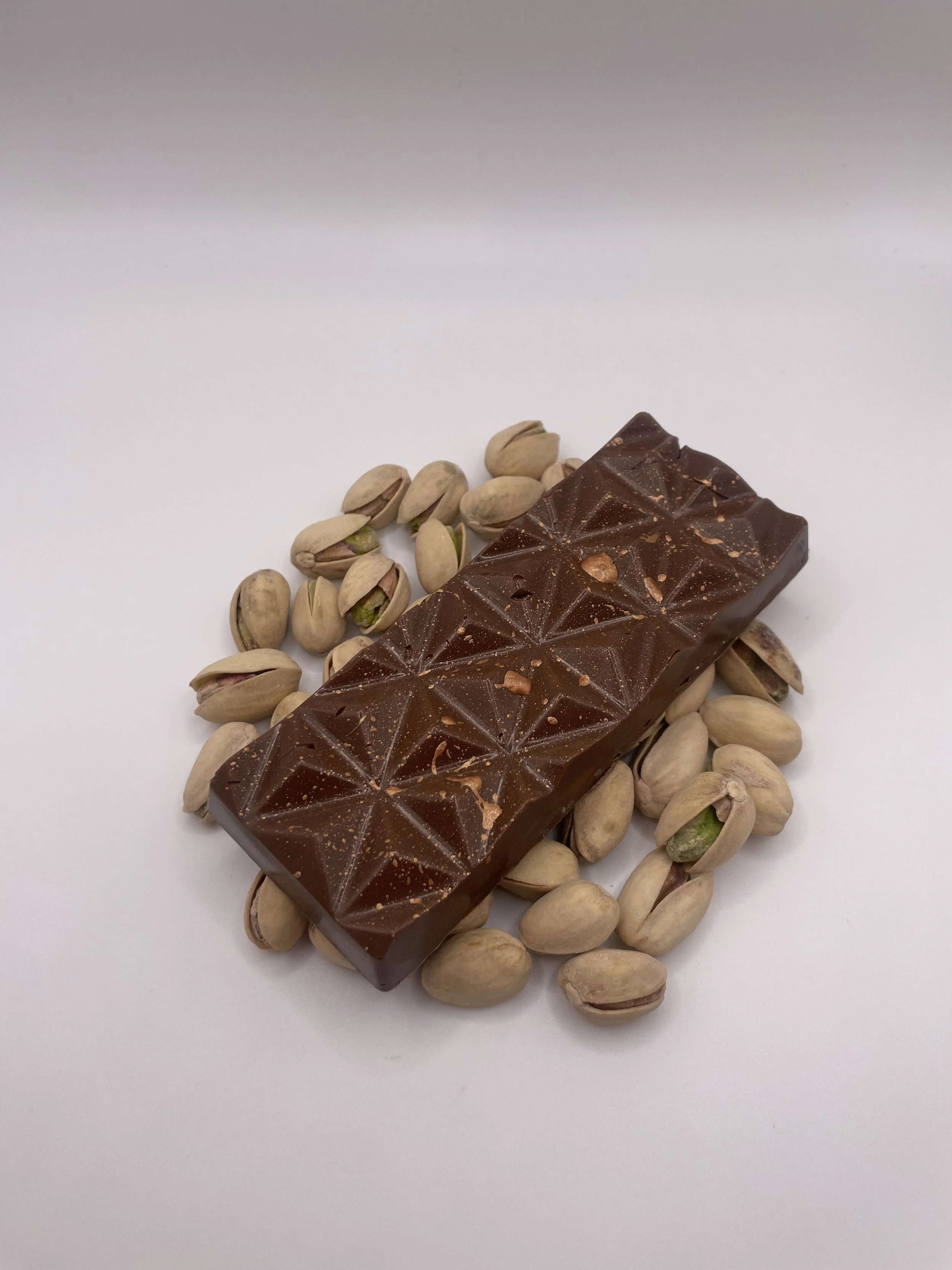 Chocolate bar surrounded by pistachio nuts on a white background.