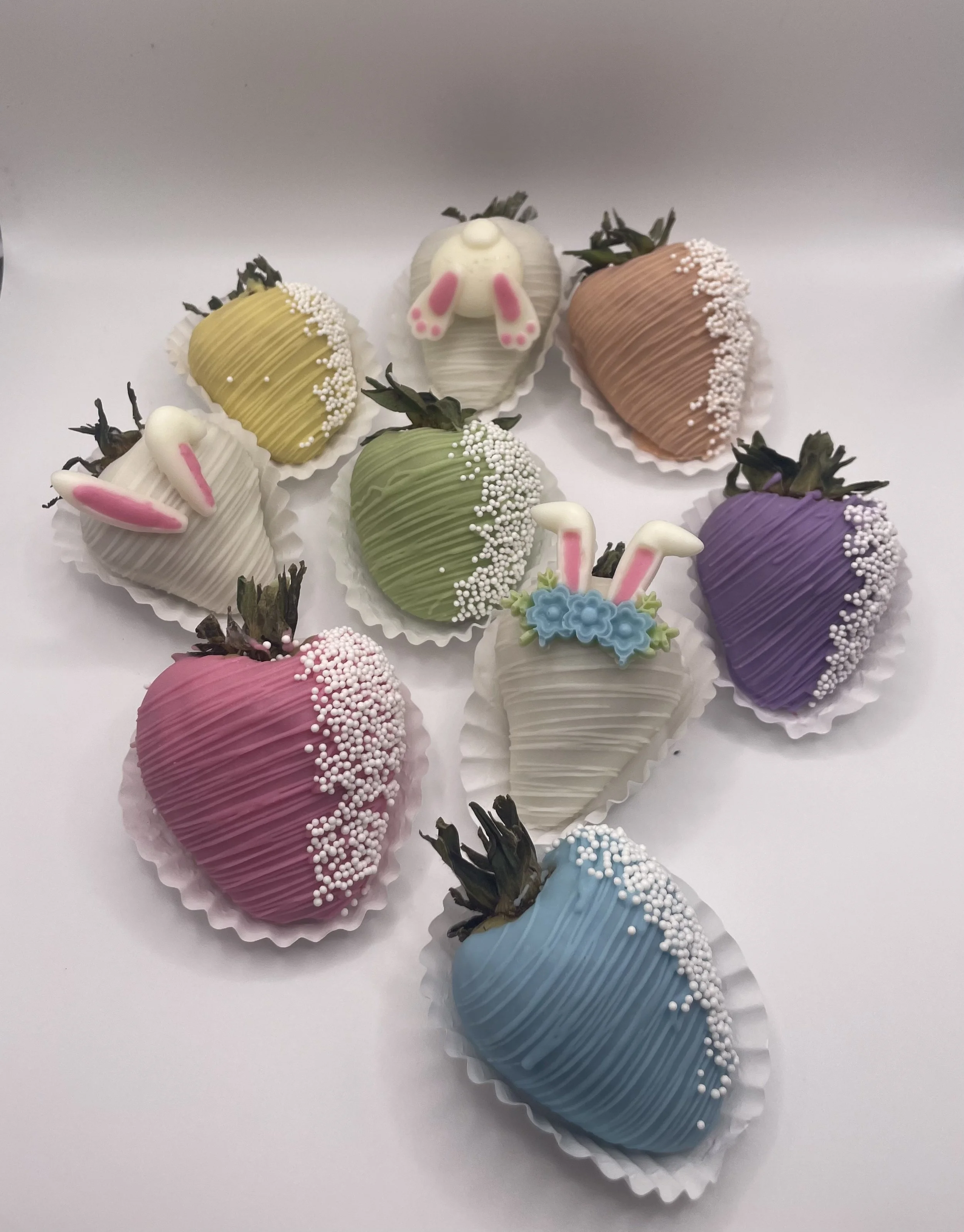 Colorful chocolate-covered strawberries decorated with bunny and Easter-themed designs and sprinkles.