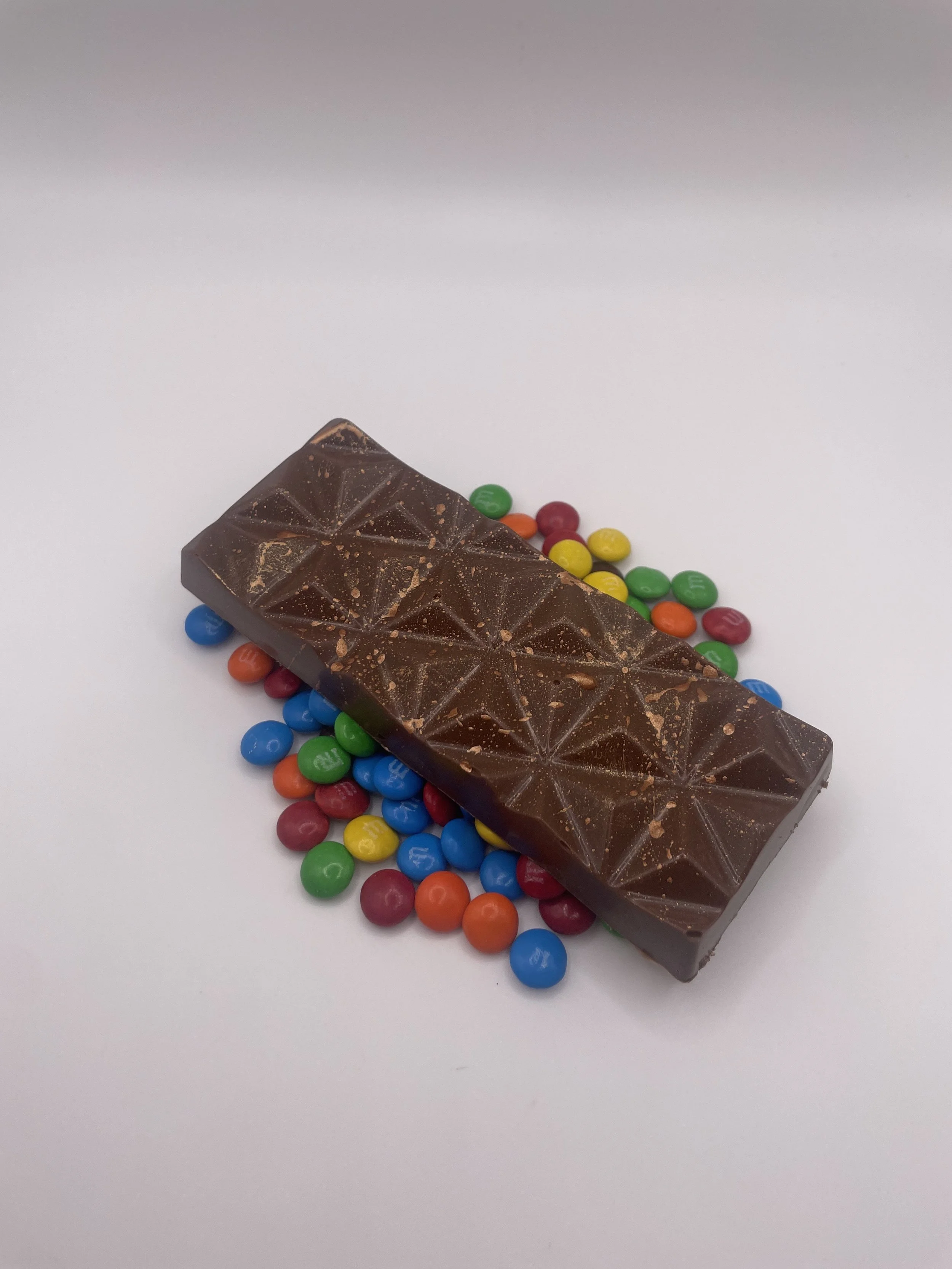 A chocolate bar surrounded by colorful candy-coated chocolates on a white background.