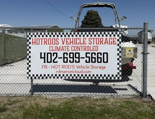 Sign on a chain-link fence advertising a hot rods vehicle storage facility with a phone number and email address
