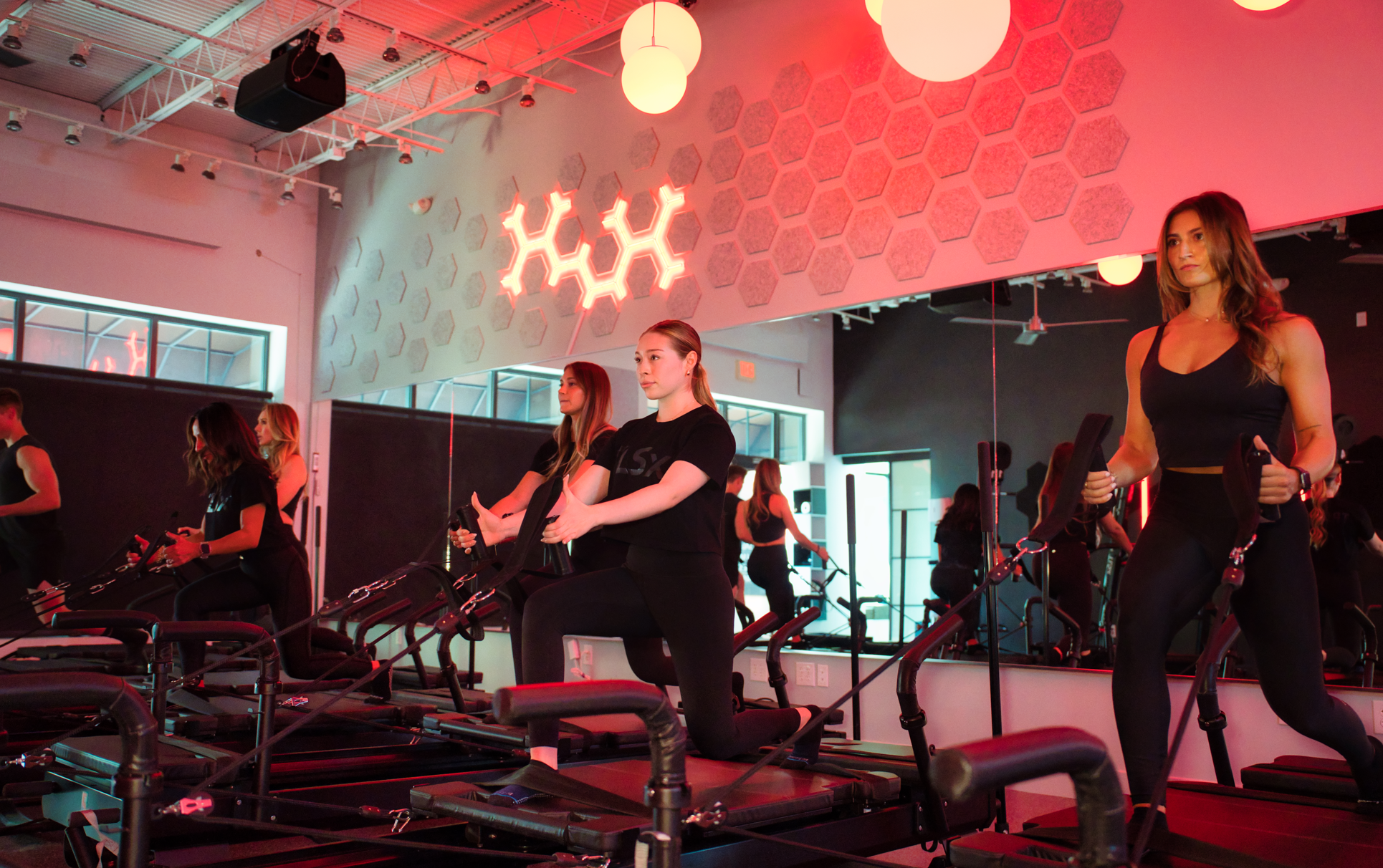 People exercising in a red-lit fitness studio using Megaformer machines.