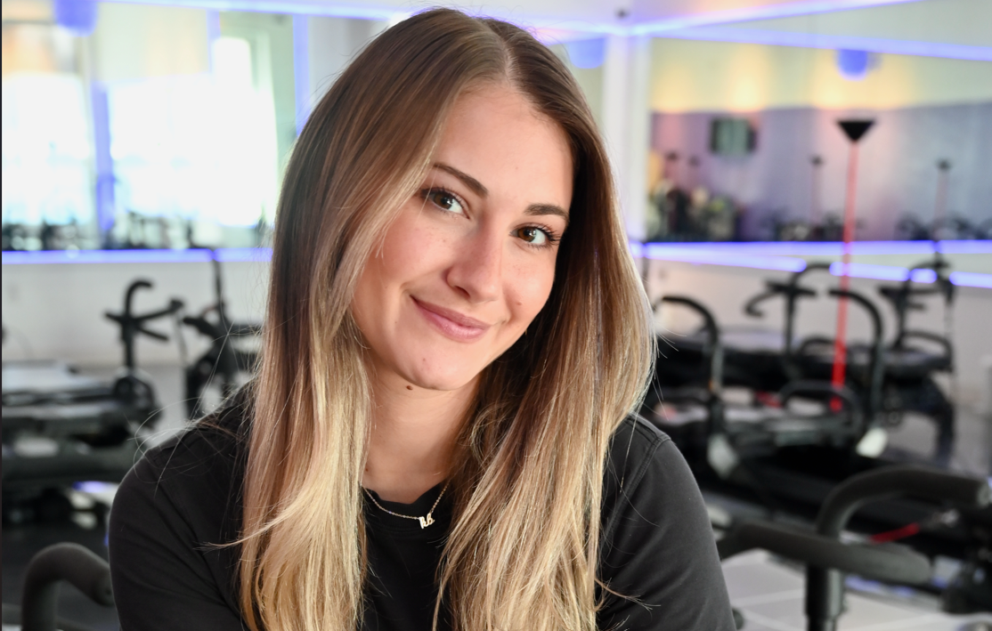 Woman smiling in gym setting with exercise equipment in background.