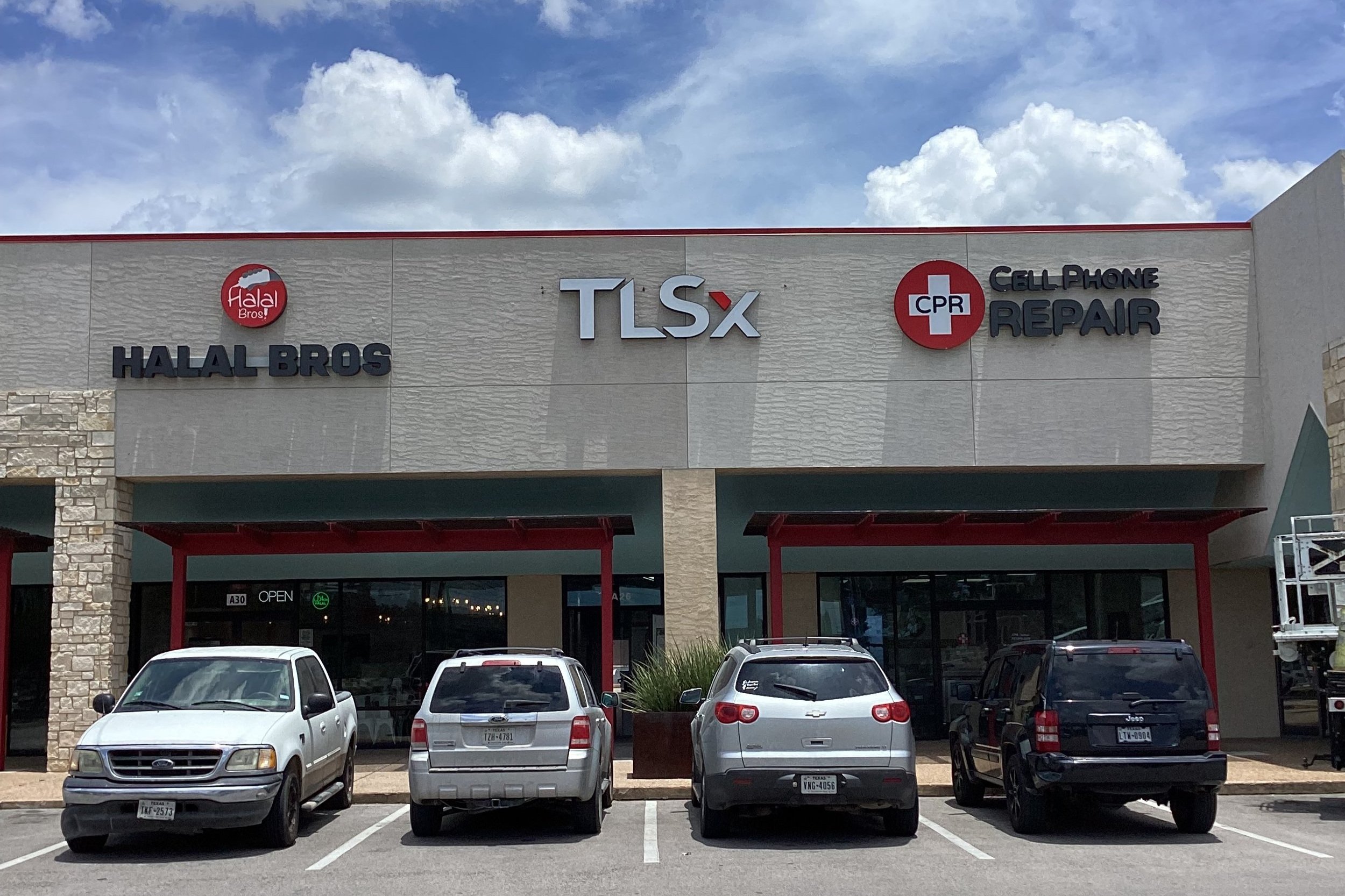 A commercial strip mall with three storefronts: HALAL BROS on the left, TLSx in the middle, and CPR Cell Phone Repair on the right. The parking lot in front has five parked cars.