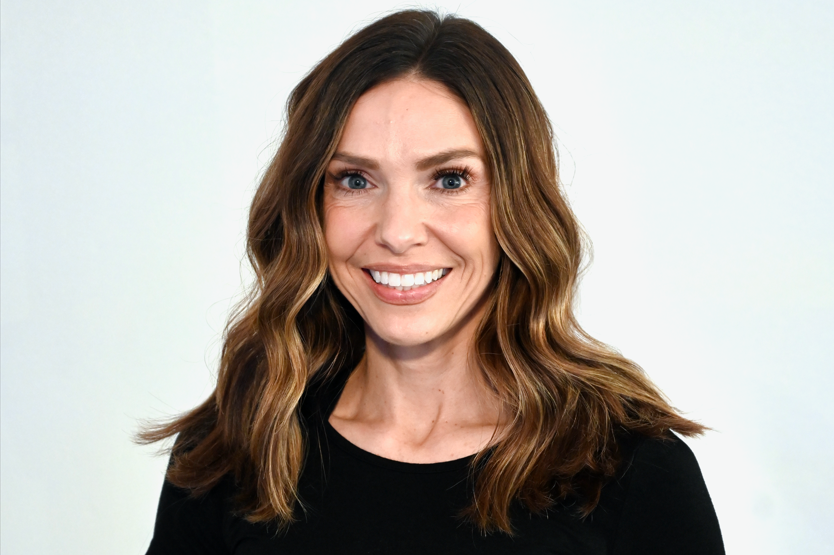 Woman with long brown hair wearing a black top smiling at the camera.