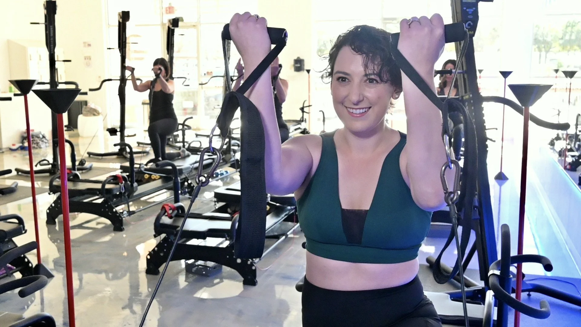 Woman exercising on fitness equipment in a gym with others in the background.