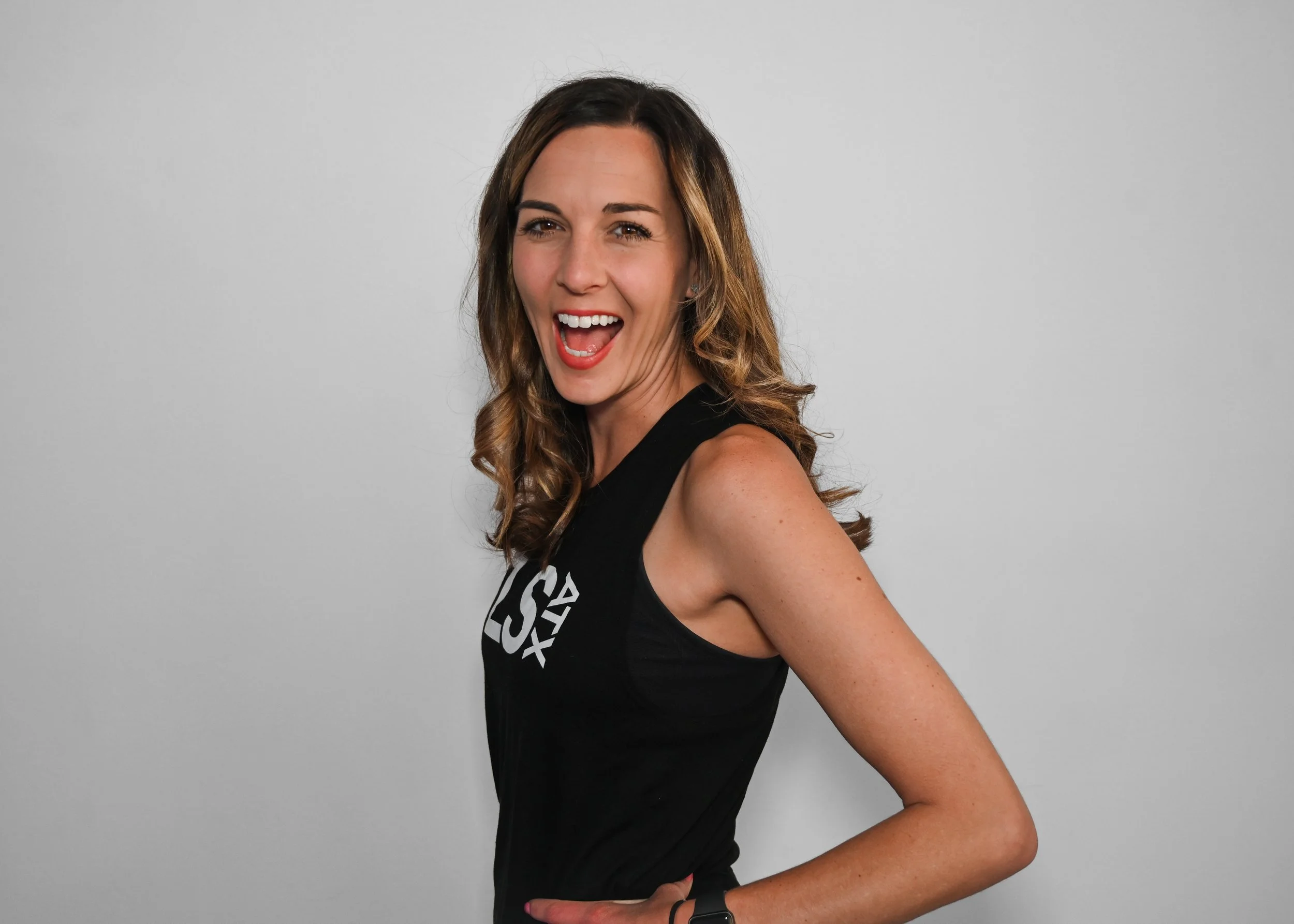 Smiling woman in black sleeveless top with wavy hair against a plain background.