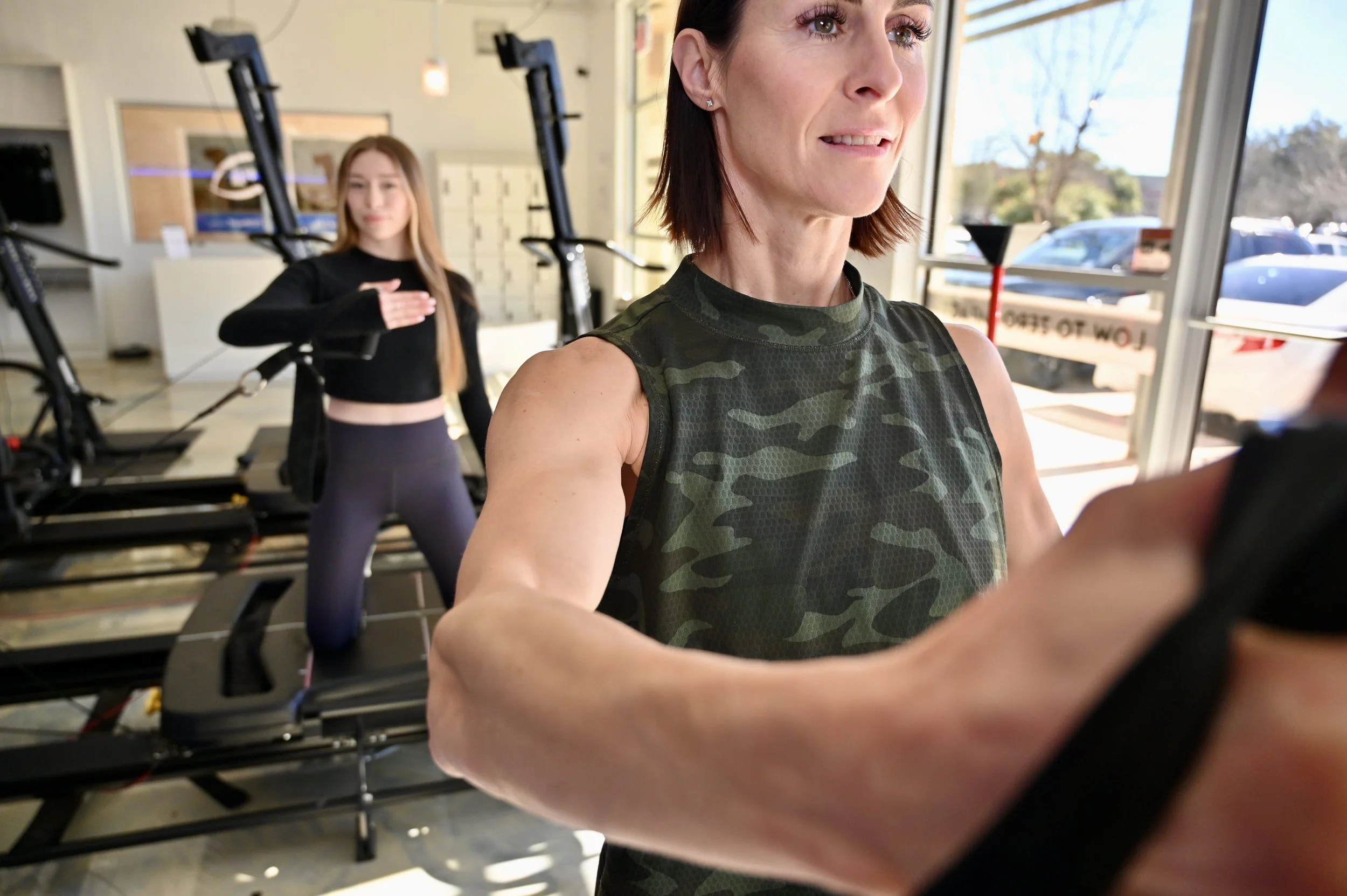Two women exercising on Pilates reformer machines in a fitness studio.