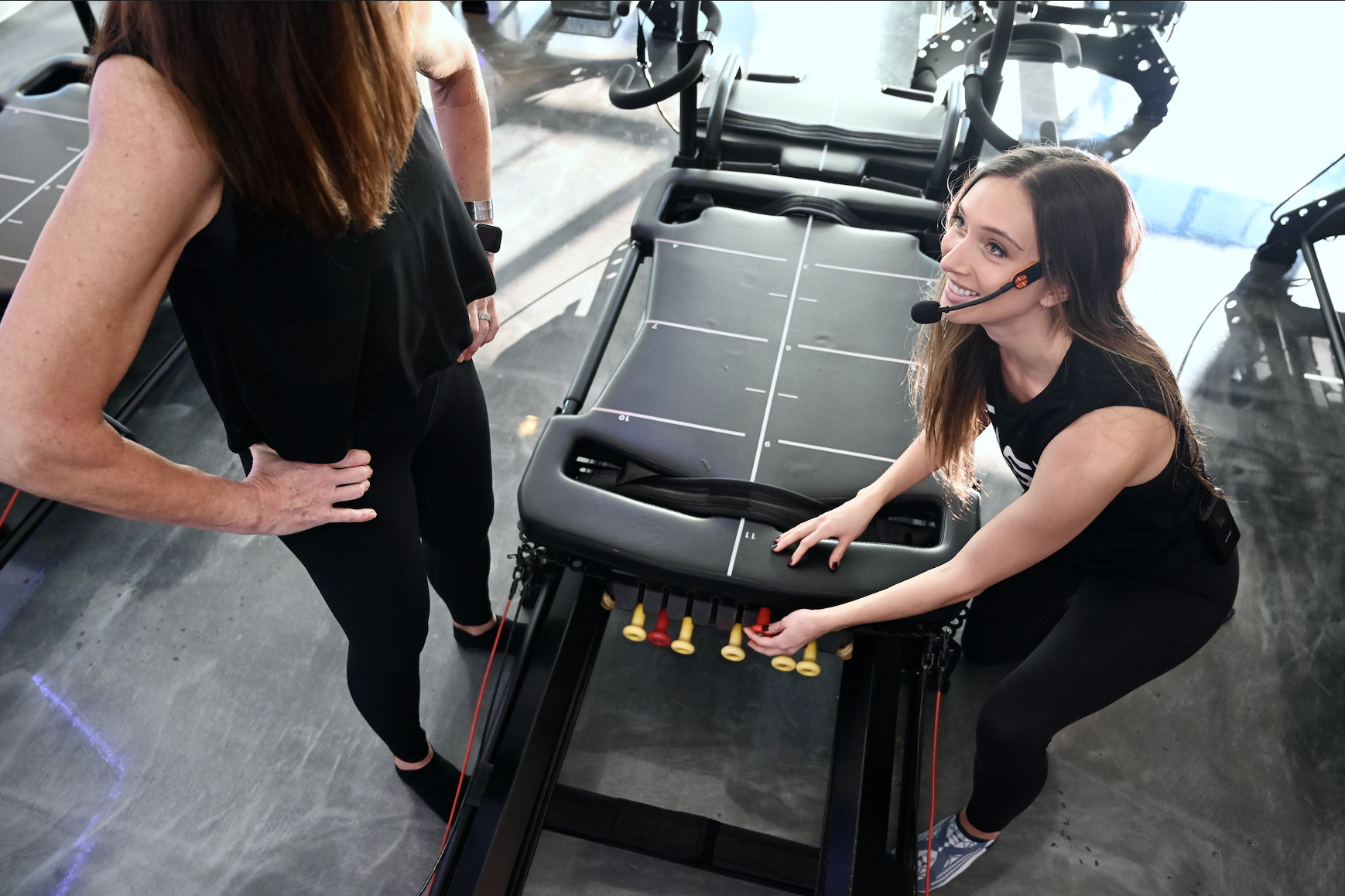 Fitness instructor adjusting a reformer machine during a workout session.