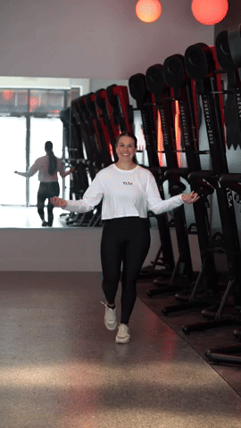 Person exercising with a jump rope in a gym, mirrored wall, exercise equipment in background.