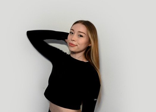 Person with long blonde hair wearing a black top posing against a plain background.