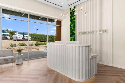 Modern office reception area with a white curved counter, large glass windows, and seating area, featuring green wall accents and minimal decor.