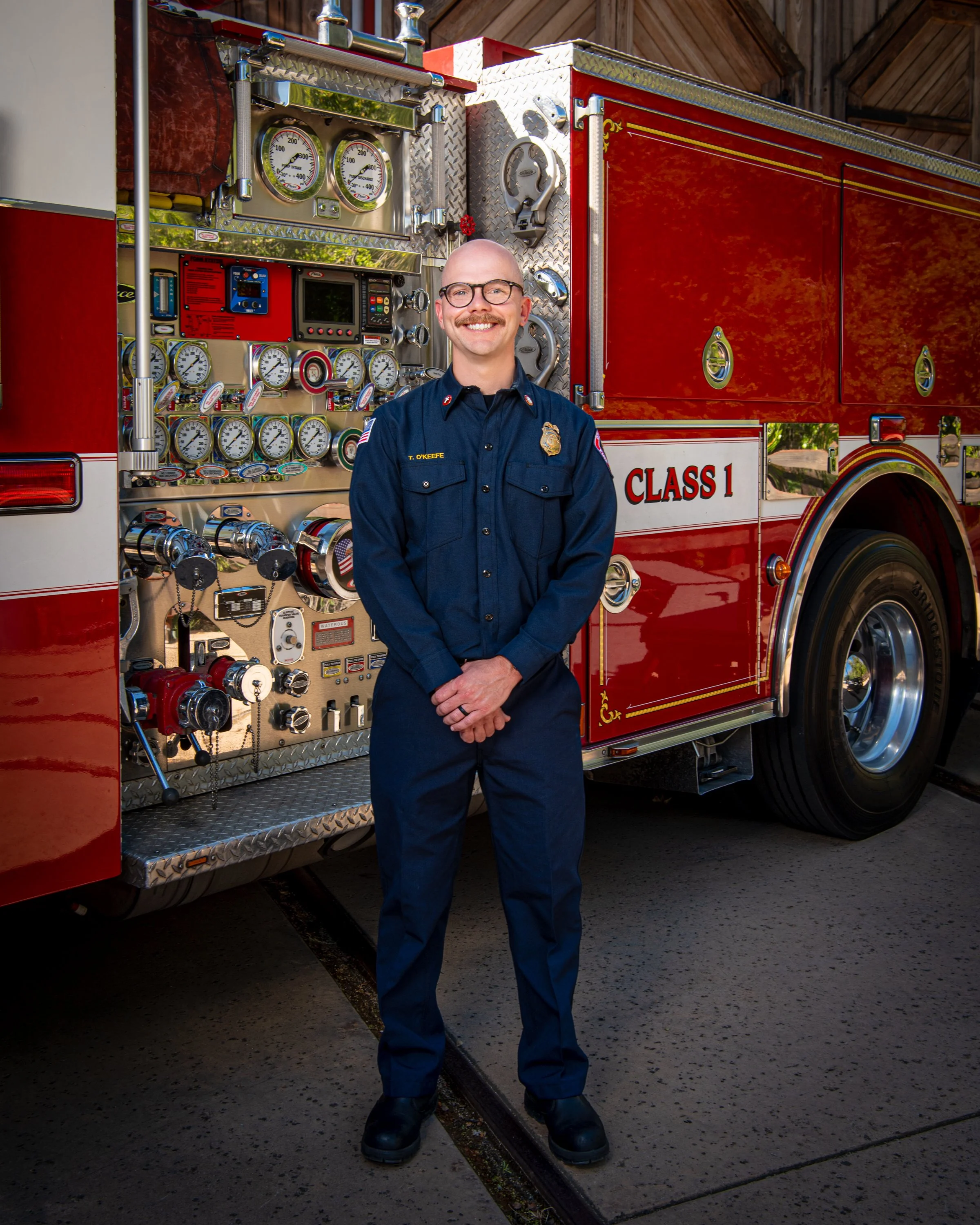 A male firefighter in uniform standing in front of a red fire truck filled with gauges and equipment.