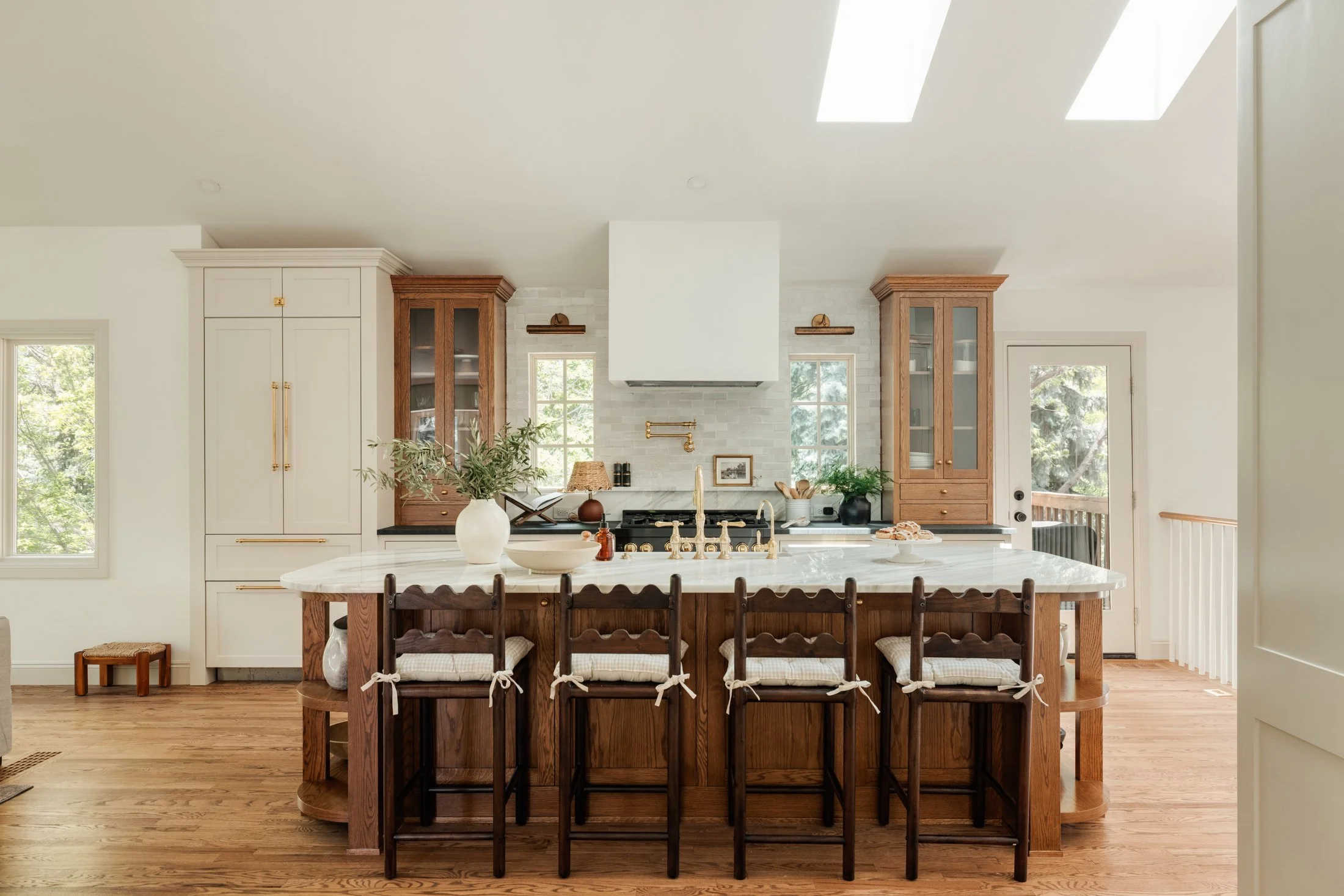 Bright kitchen with white cabinets, wooden accents, a large marble island, and four chairs with woven seats.