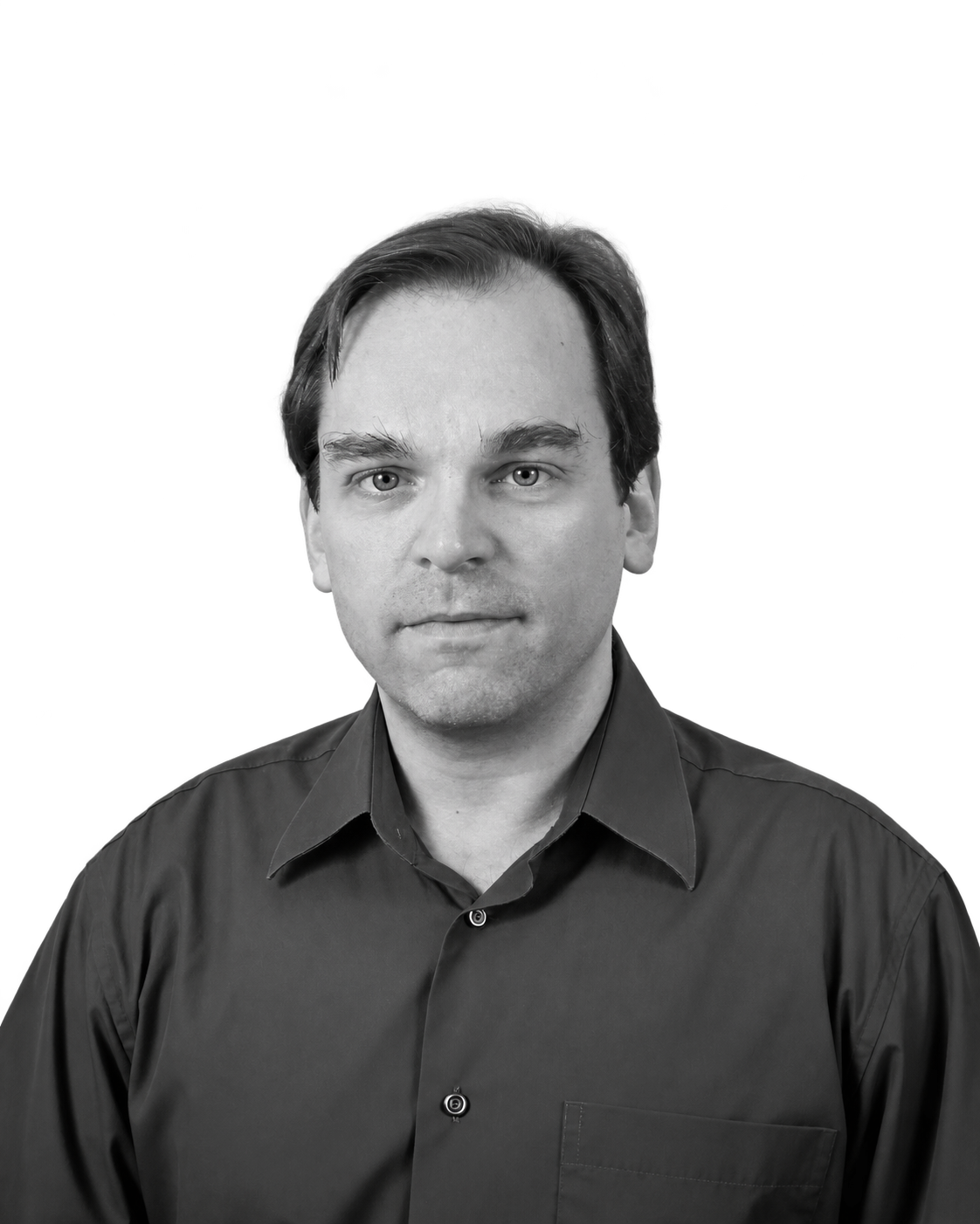 Black and white portrait of a man with short, dark hair, wearing a dark, button-up shirt, looking directly at the camera with a neutral expression.