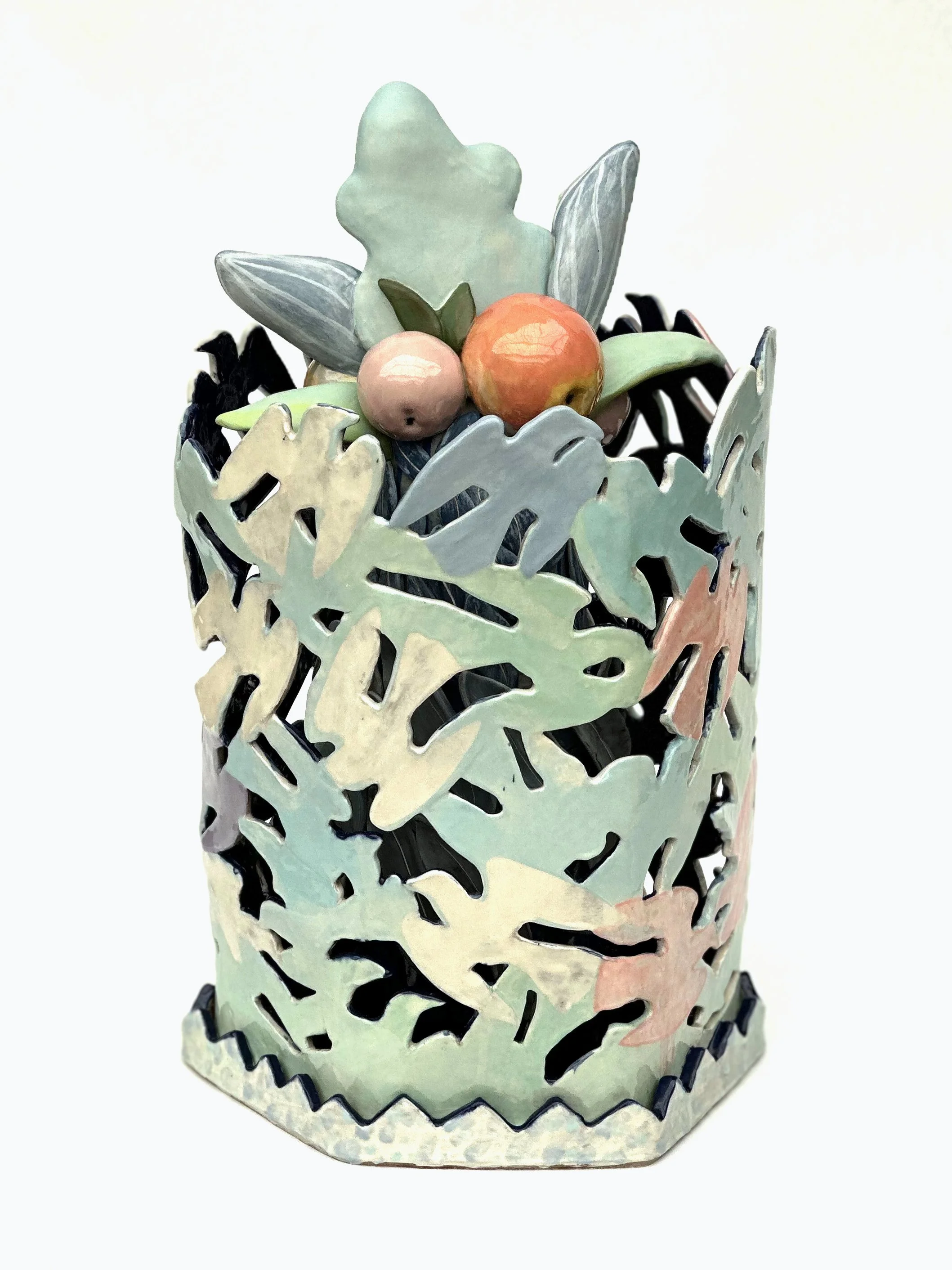 Decorative metal container with cut-out leaf pattern, filled with artificial fruit and leaves.