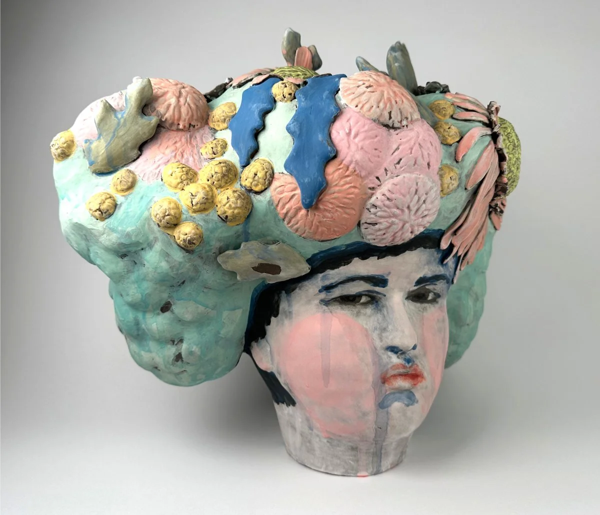 Ceramic sculpture combining a human face with a large, colorful, botanical-inspired headpiece.
