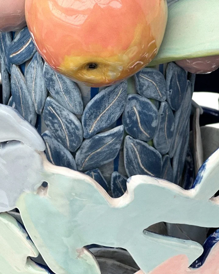 Close-up of ceramic art featuring a peach, blue leaves, and pastel-colored elements.