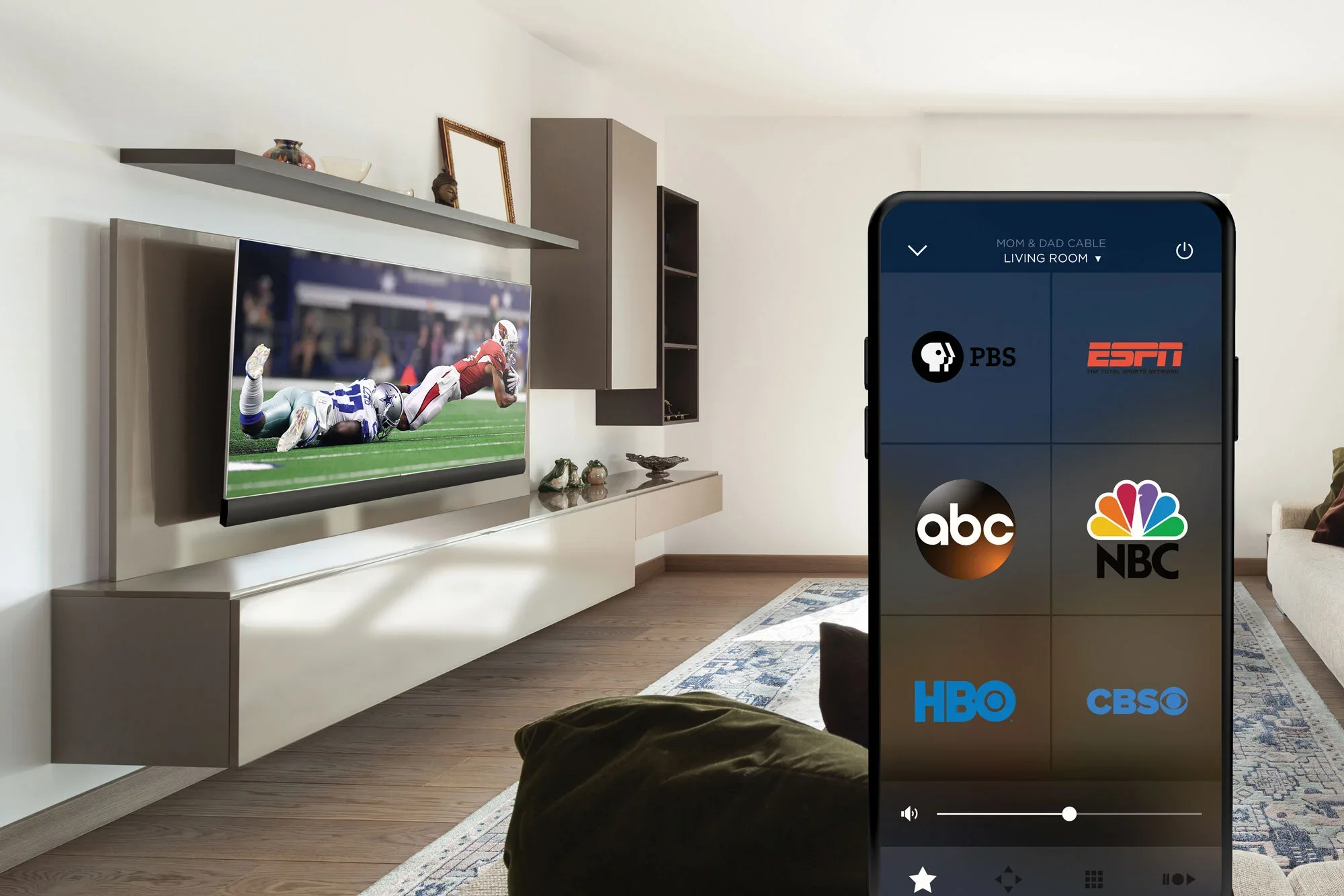 Living room with mounted flat-screen TV showing football game, and a smartphone with streaming app interface displaying TV channel options.