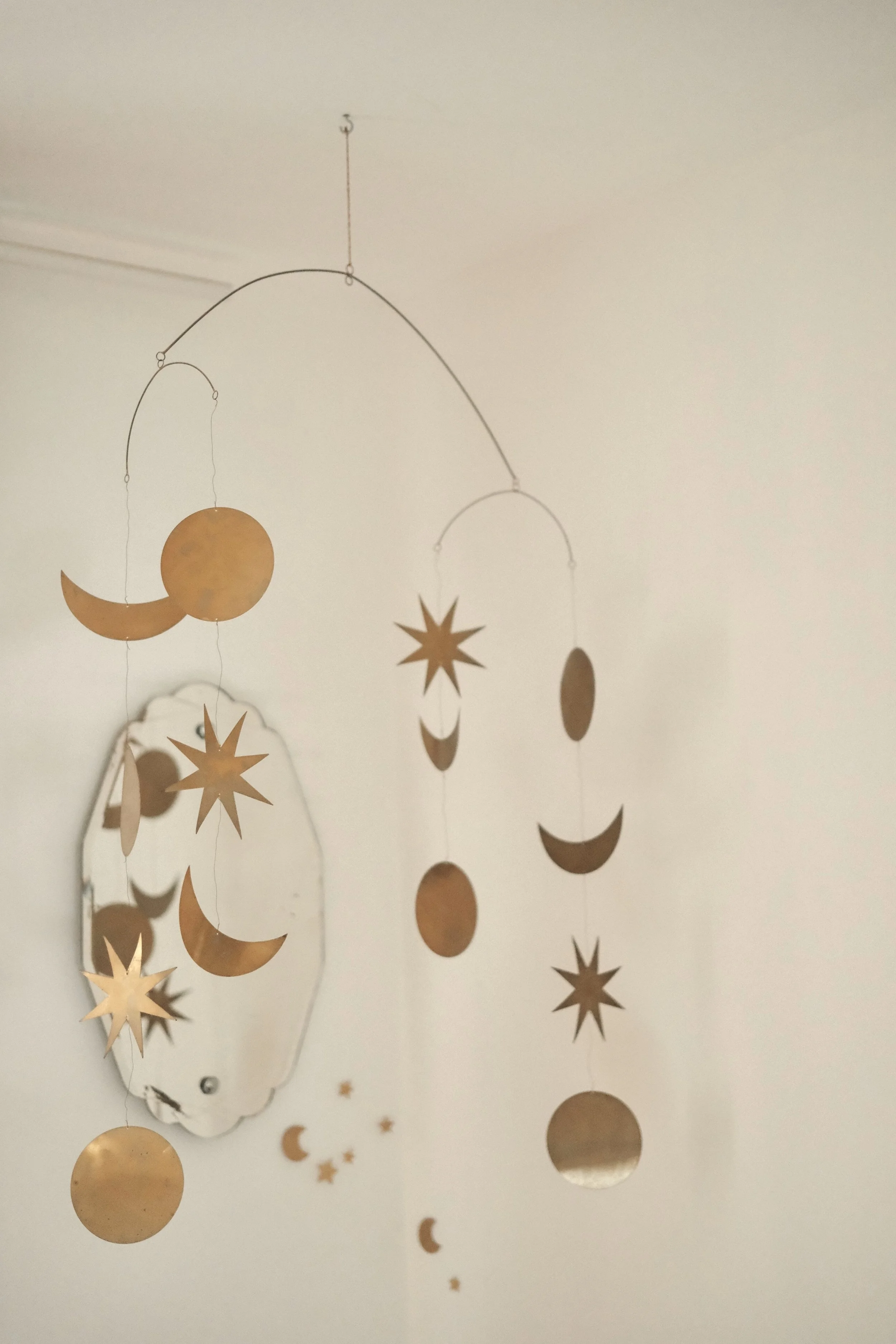 Decorative hanging mobile with gold-colored crescent moons, stars, and circles, with a mirror mounted on a wall in the background.