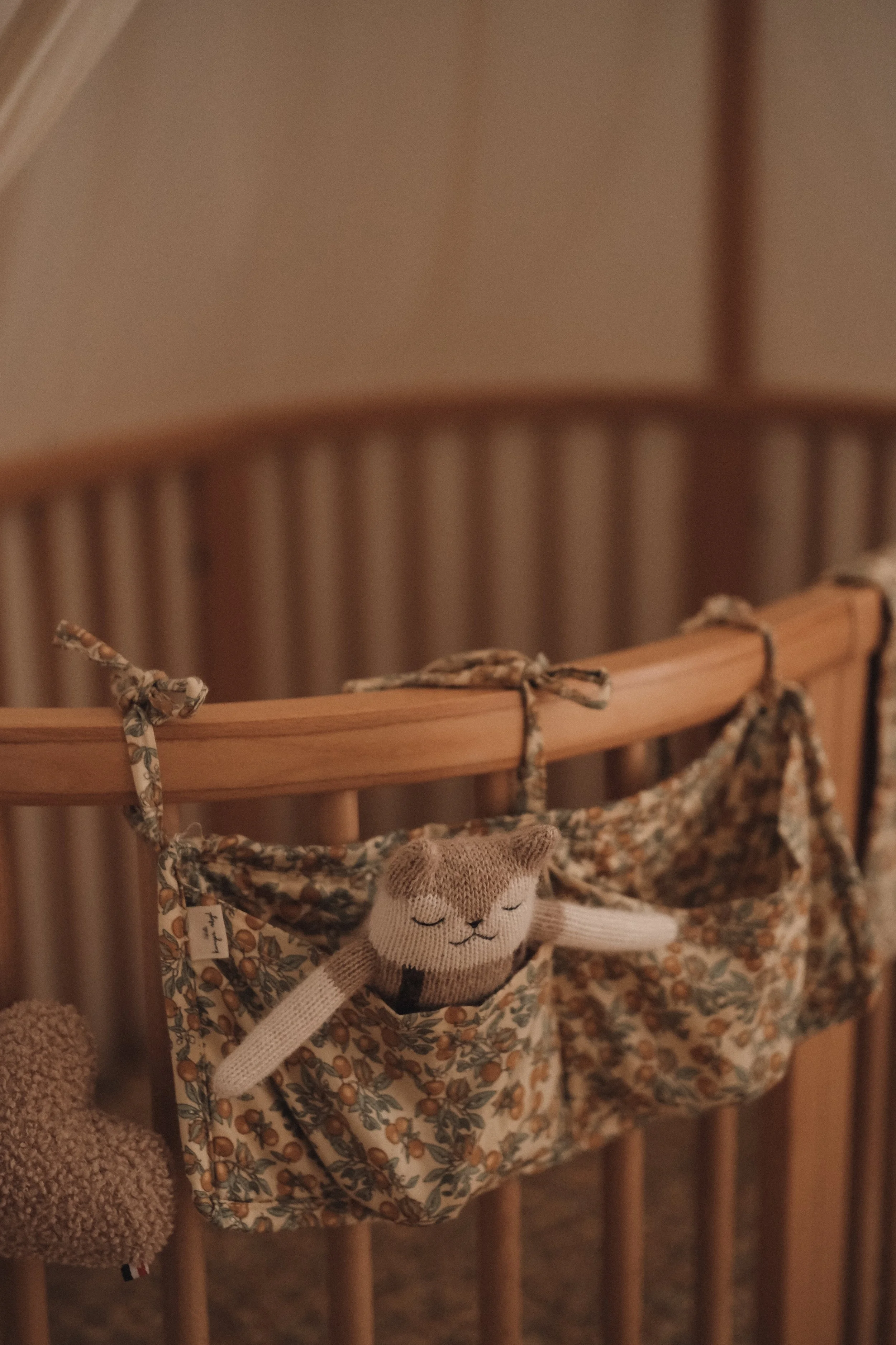 A baby crib with a floral hanging organizer that has a stuffed sock puppet in the shape of a smiling bear in a sleeping pose.