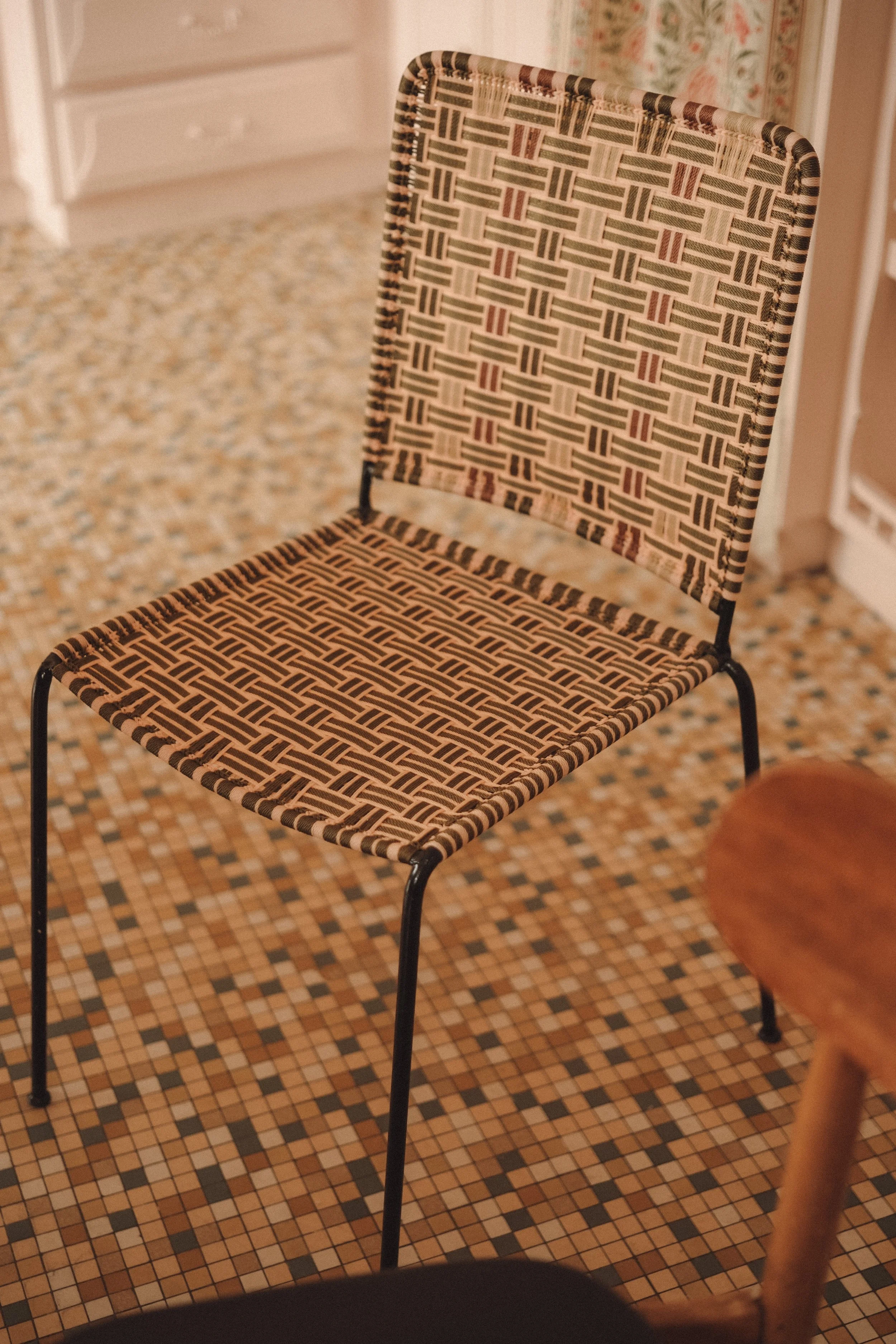 A vintage woven chair with a patterned fabric seat and backrest, standing on a mosaic tile floor in a cozy room.