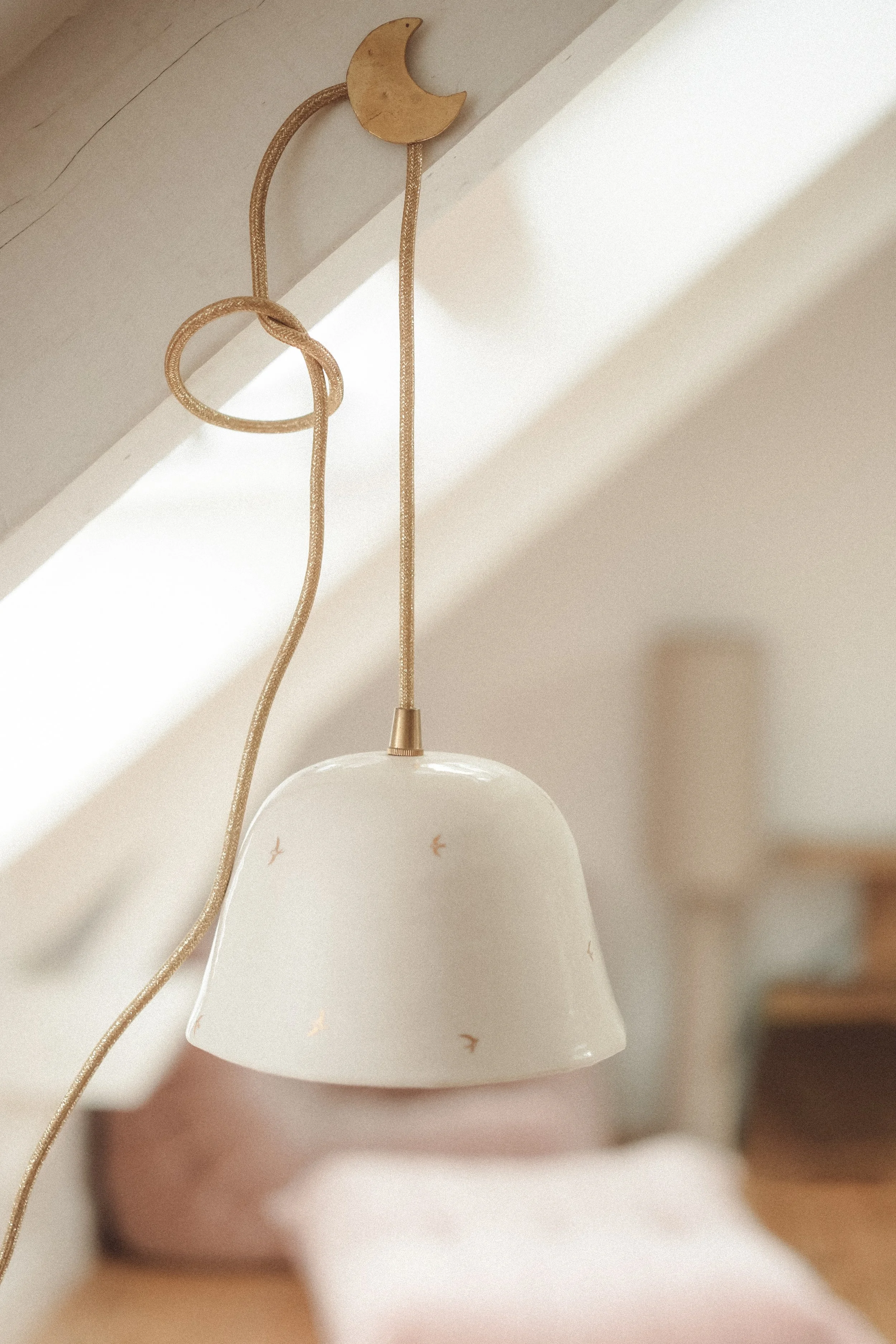 A ceiling-mounted lampshade hanging from a gold cord against a sloped ceiling.