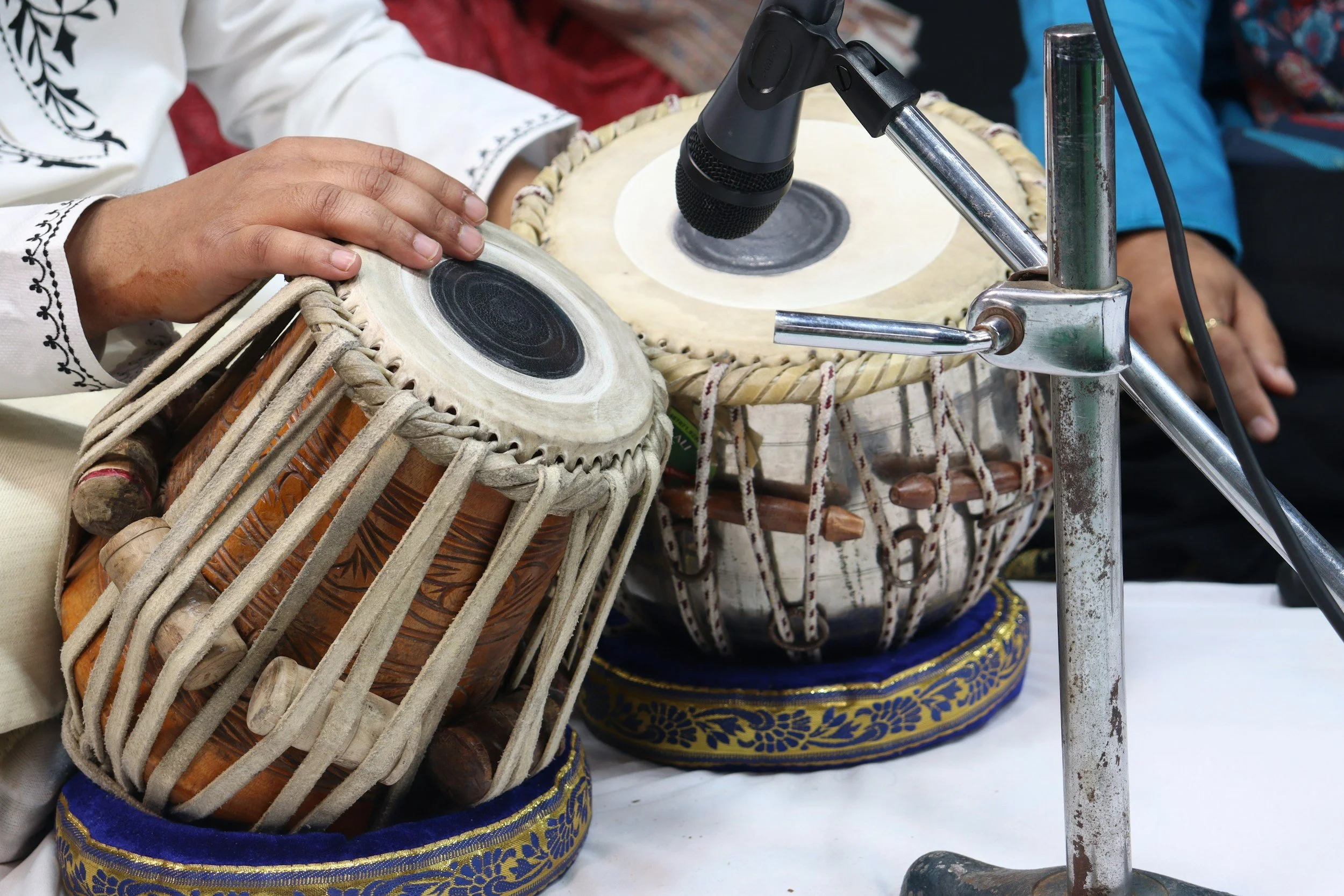 A man playing a tabla drum set that is under nearth a microphone.