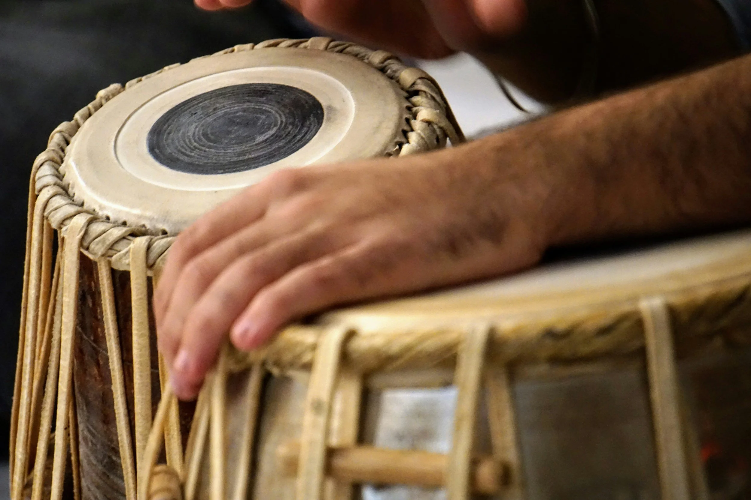 Close-up of a person's hand playing a tabla drum, with a focus on the drumhead and the woven rim.