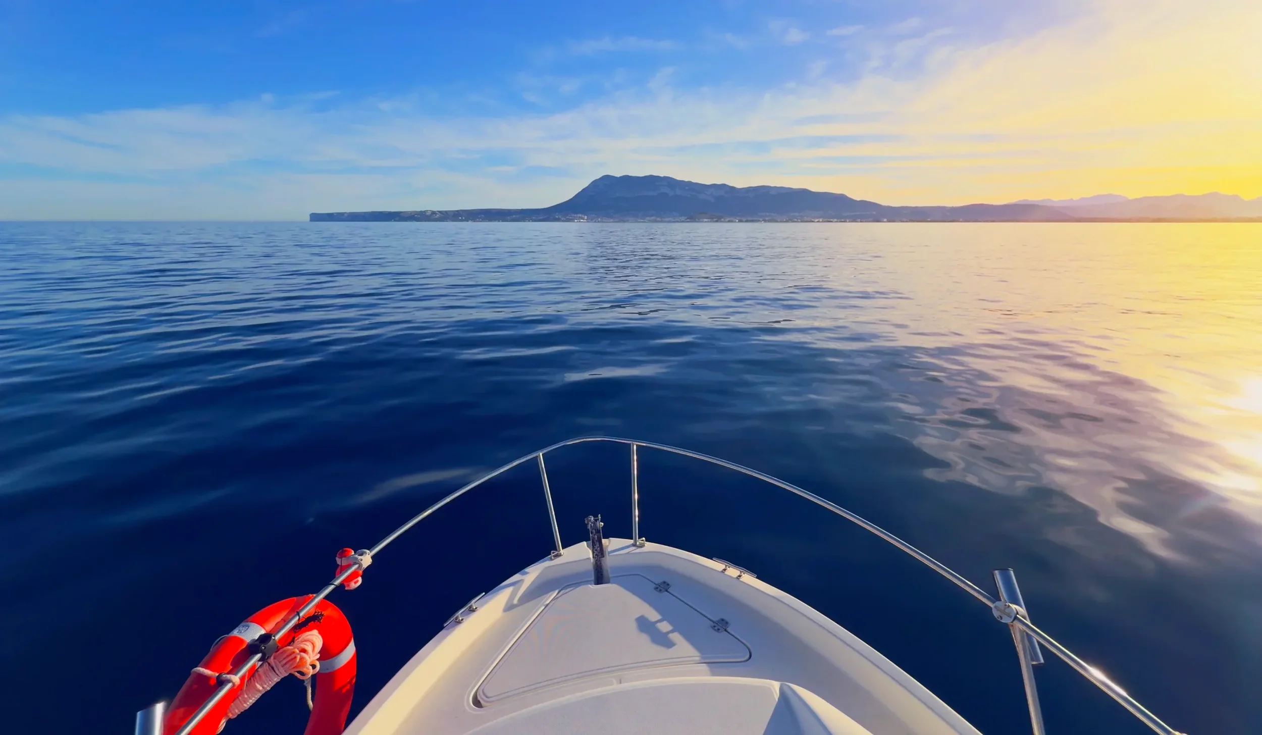 Charter con proa del barco navegando al atardecer frente a la costa de Denia