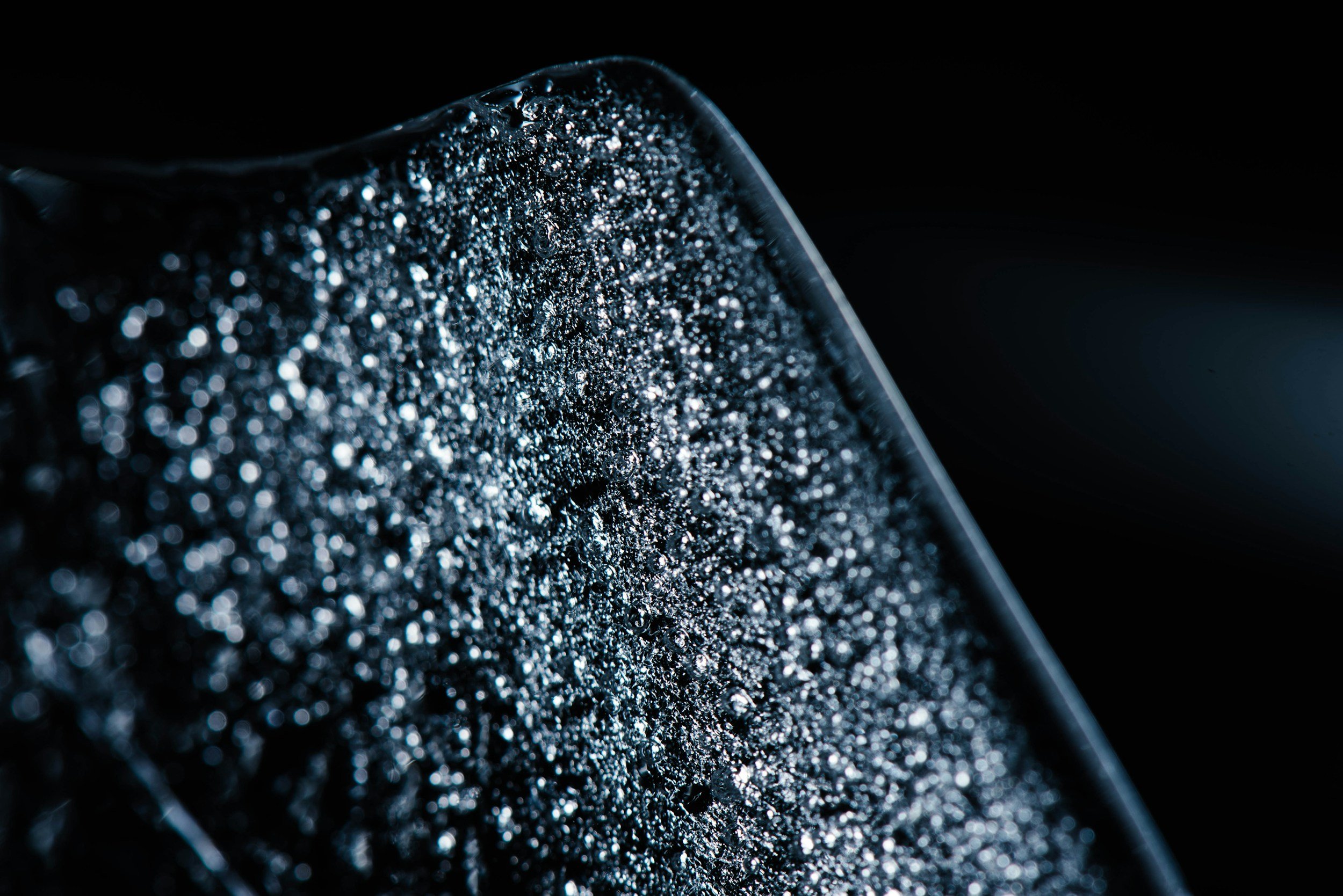 Close-up of water droplets on a black surface with a blurred dark background.