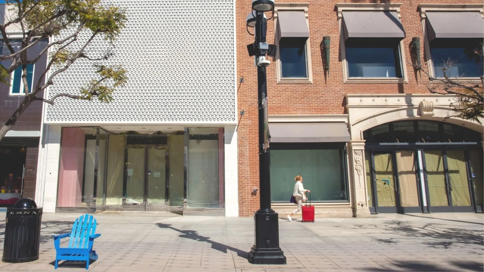 An empty blue chair on Third Street Promenade in Santa Monica, in front of vacant storefronts with papered-over windows.