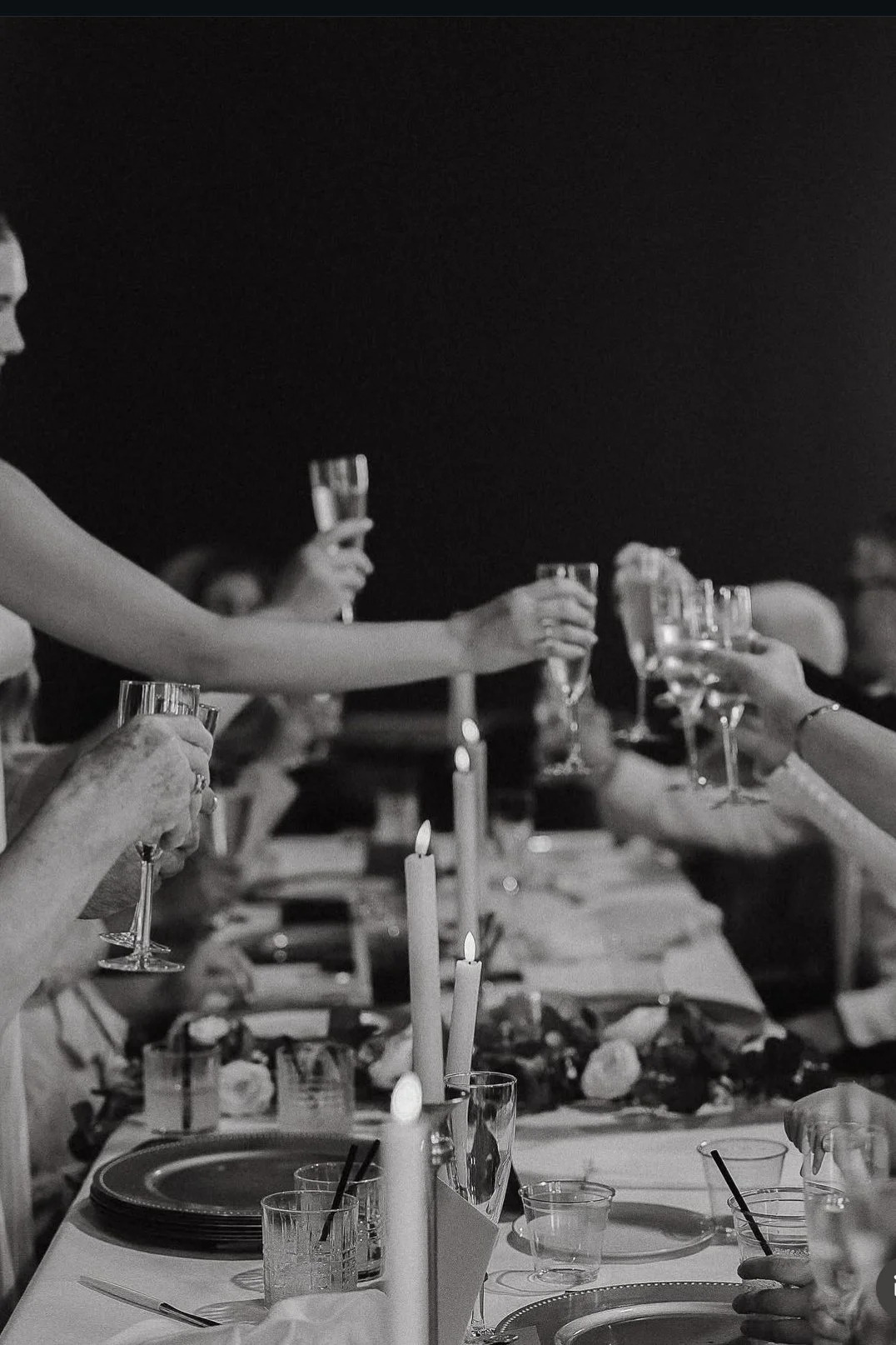 People raising champagne glasses during a dinner celebration at a long table with candles and plates.