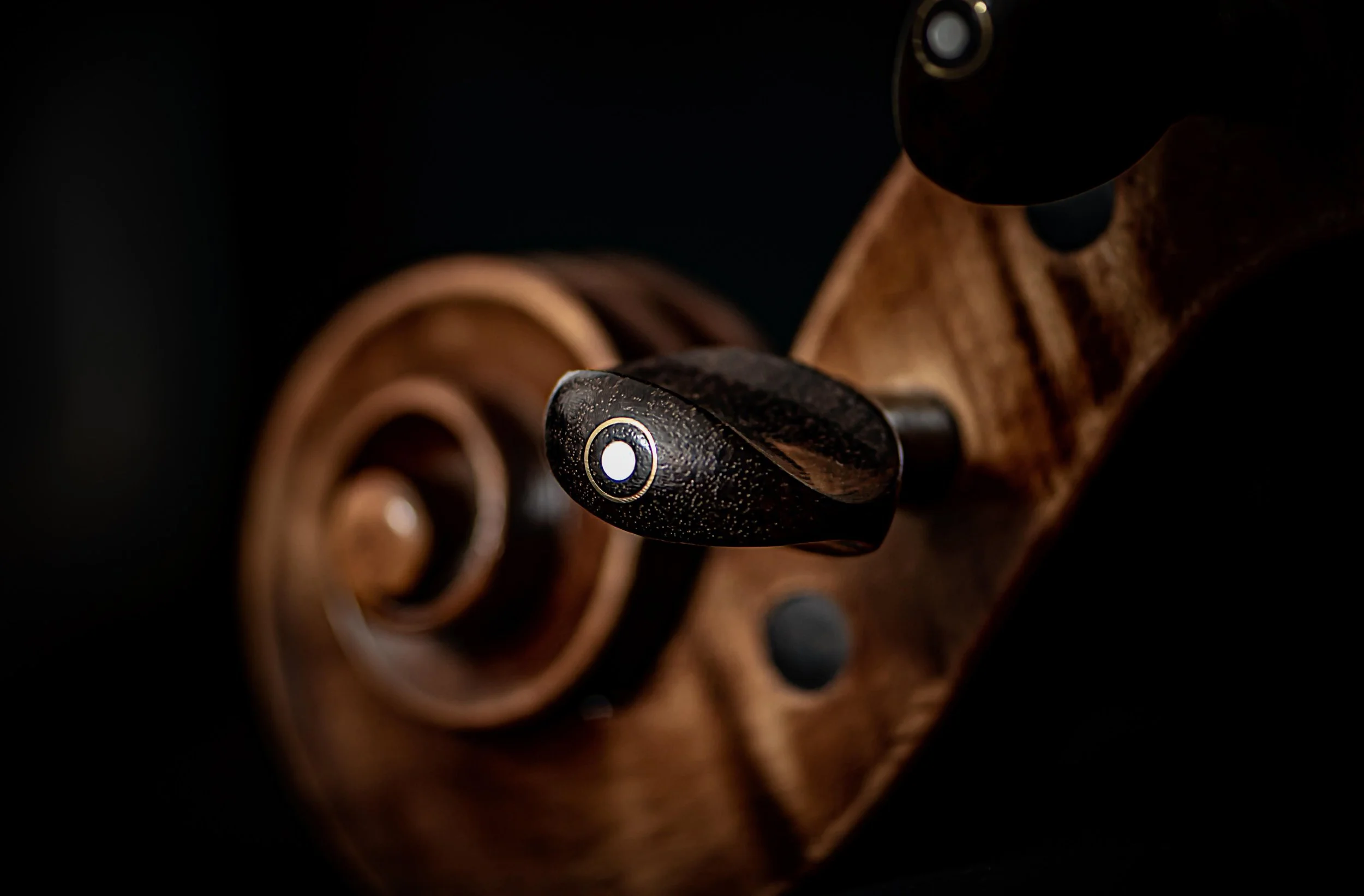 Close-up of a vintage wooden rotary telephone dial with a black finger stop and beige finger wheel against a dark background.