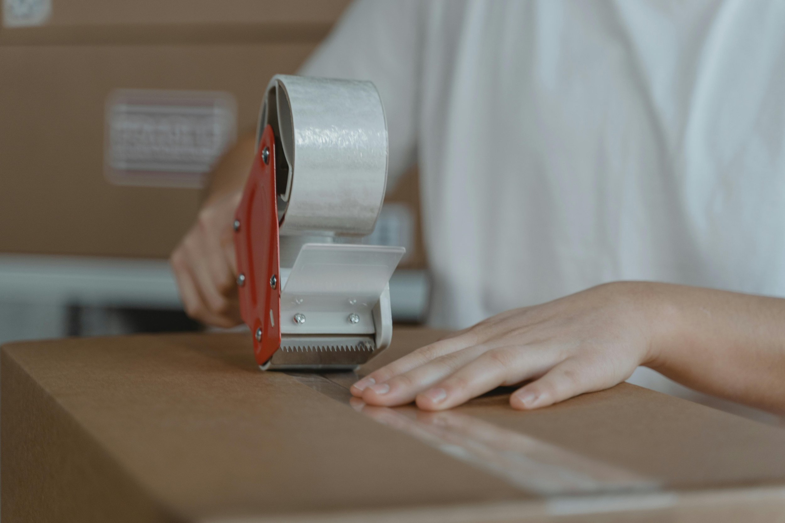 A person uses a tape dispenser to seal a cardboard box.