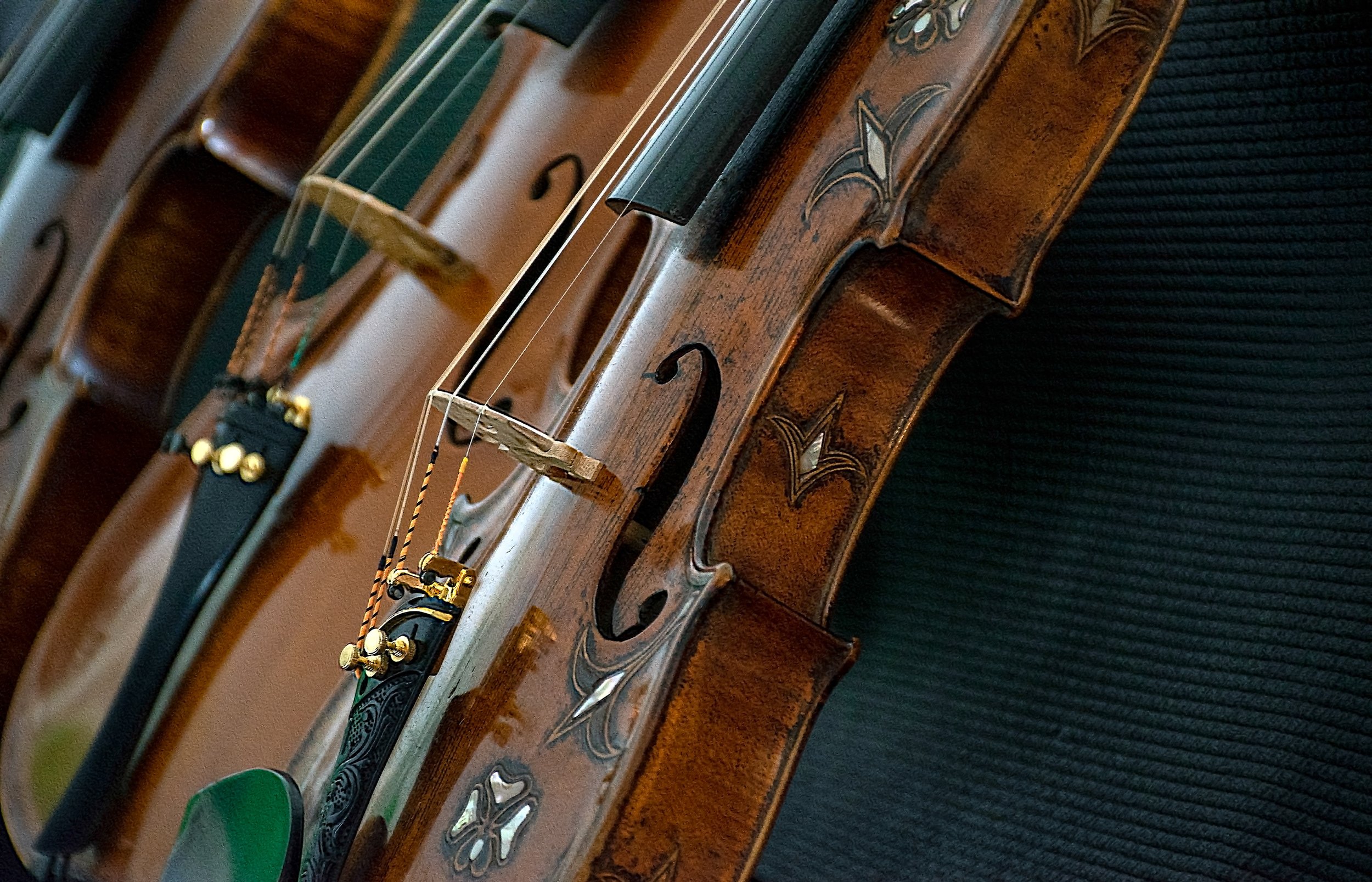 Close-up of violins with detailed wood grain and decorative inlays on a black textured background.