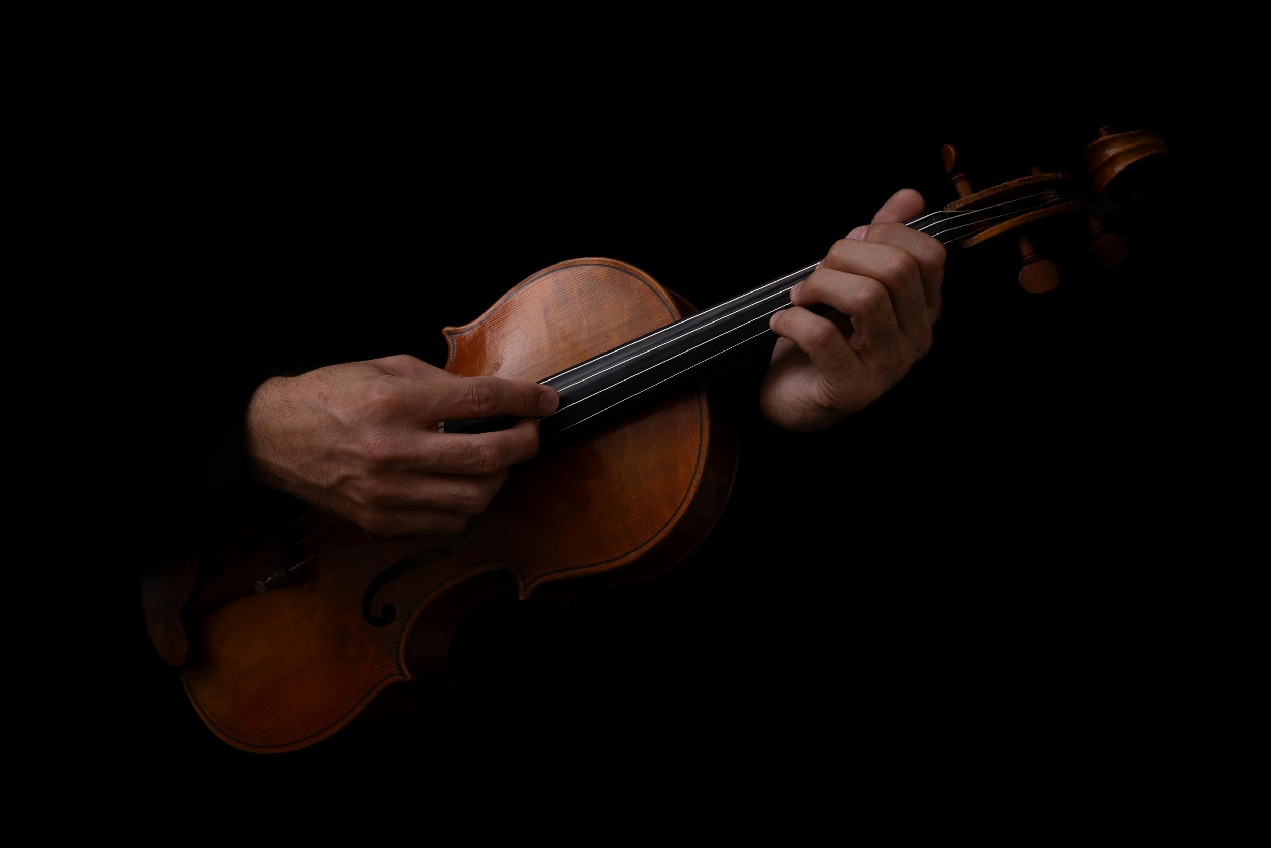 Person playing a violin against a black background.