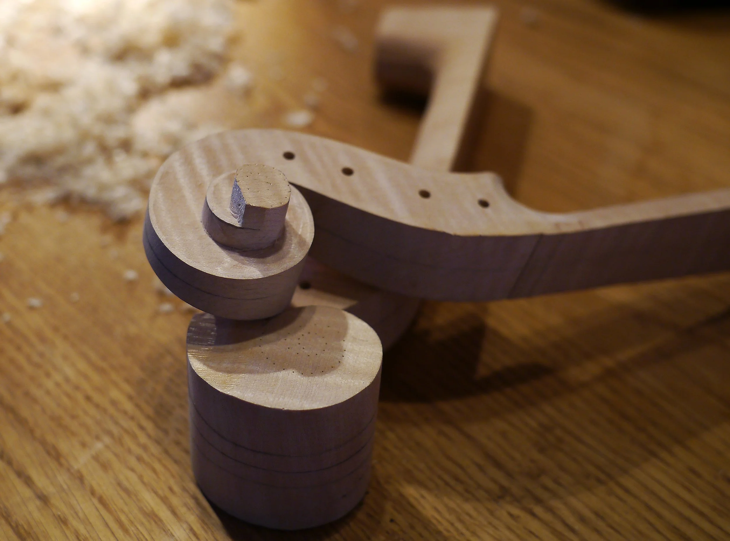 Close-up of wooden toy wheels and a connecting wooden piece on a wooden surface, with wood shavings in the background.