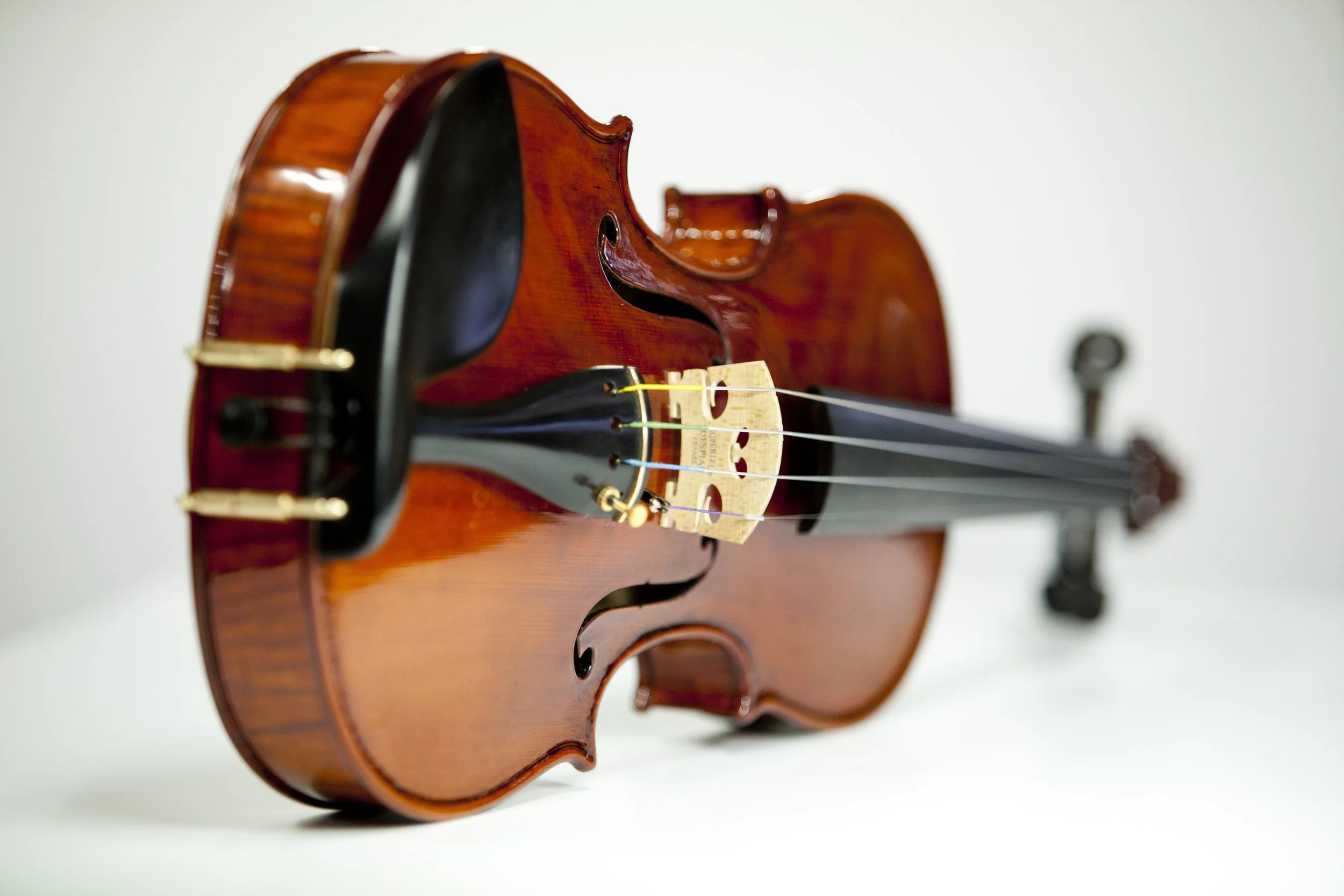 Close-up of a violin lying on its side with the strings and bow clamp visible against a plain white background.
