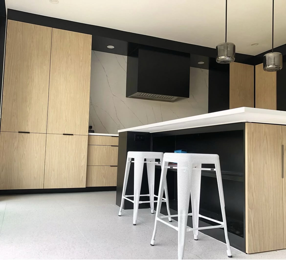 Modern kitchen with light wood cabinets, white marble backsplash, black accents, and white barstools at a black and white island.