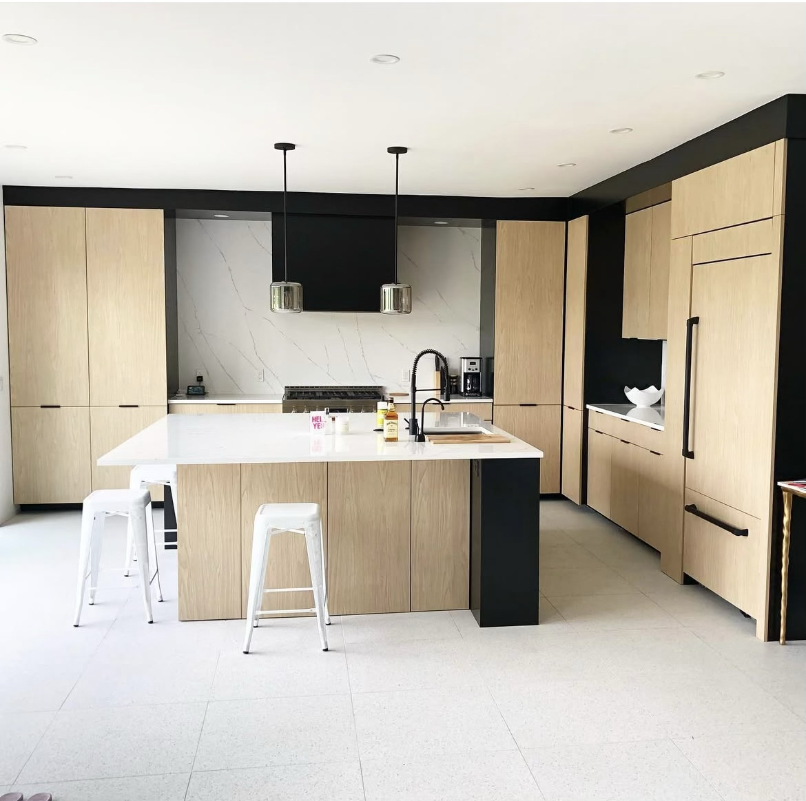 Modern kitchen with light wood cabinets, white island with seating, black accents, and stainless steel appliances.