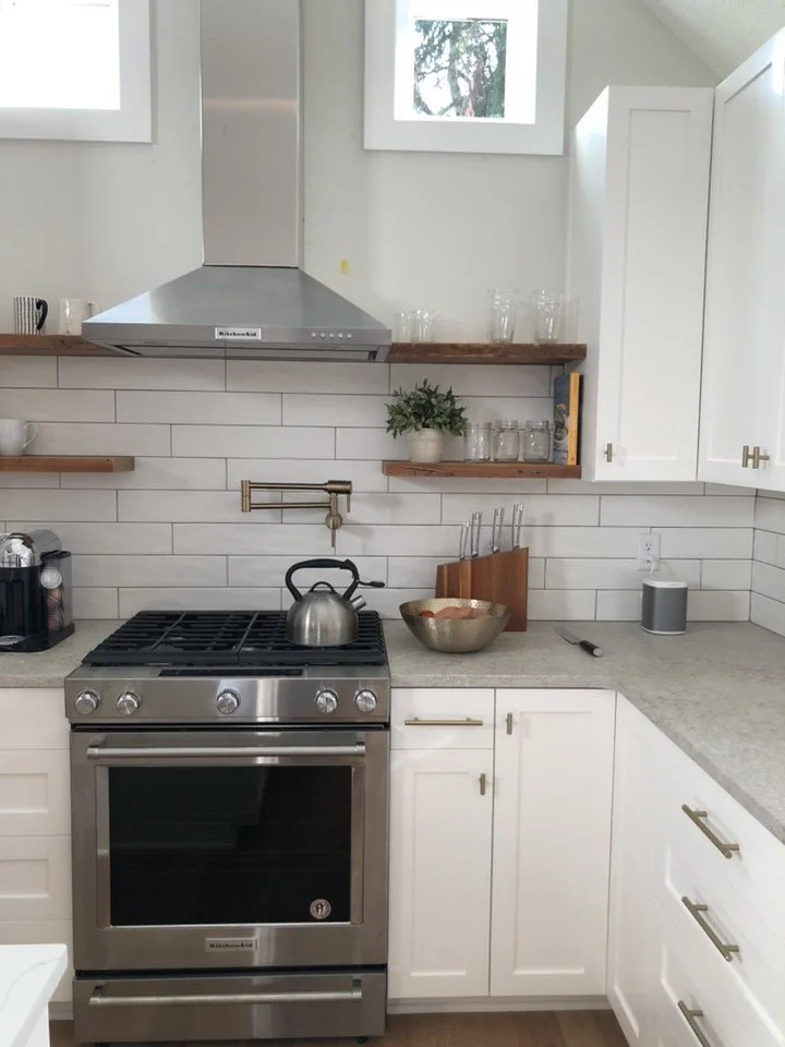 Modern kitchen with stainless steel stove, white cabinets, wooden countertops, glass jars, potted plant, and wall-mounted faucet.