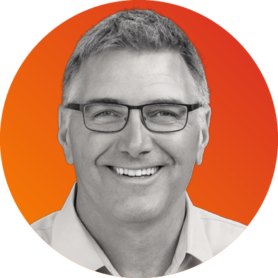 A smiling man with short gray hair and glasses, wearing a light-colored shirt, set against an orange background.